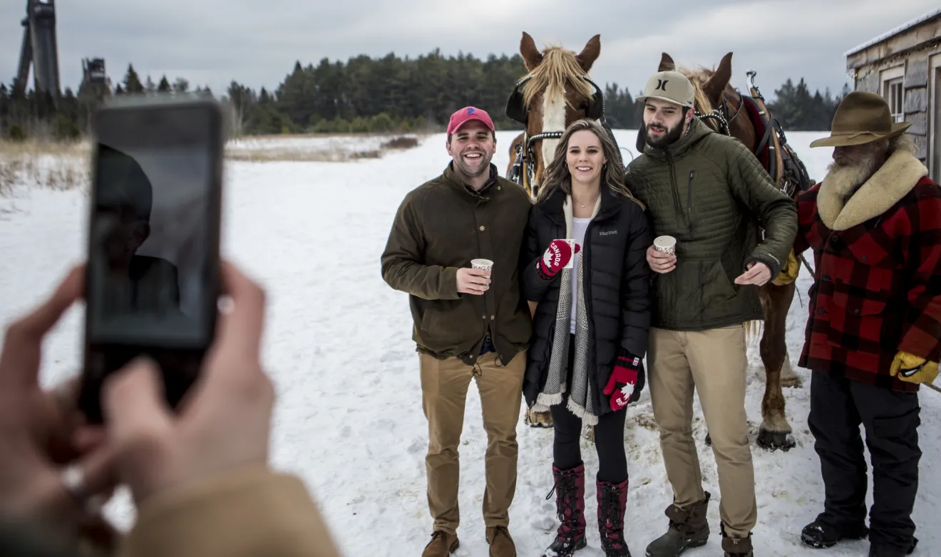 A group of people get their picture taken in front of a horse drawn sleigh