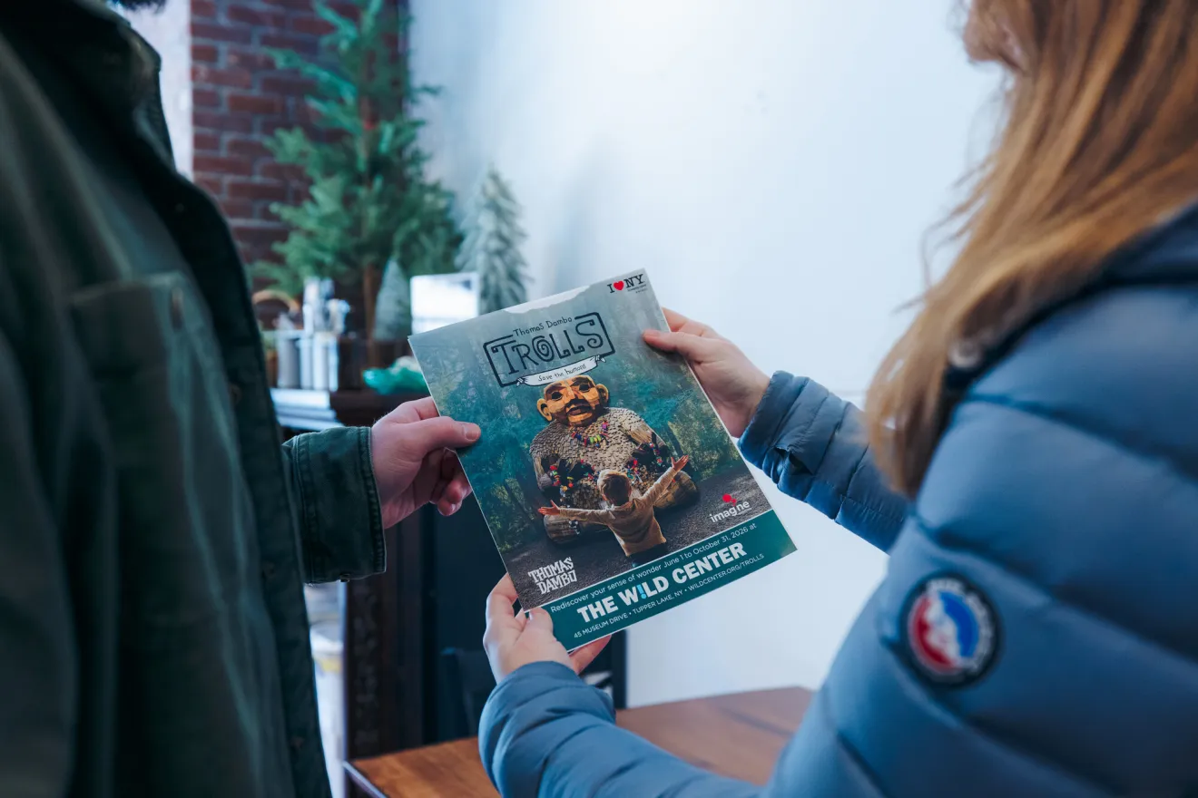 A man and woman look at a brochure of a wooden troll exhibit.