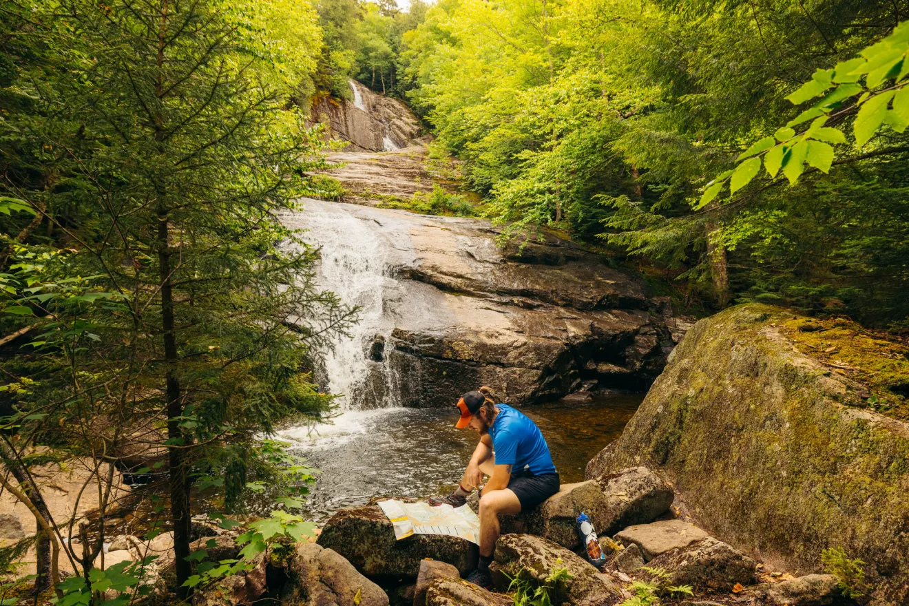 A man reads a map next to a waterfall.