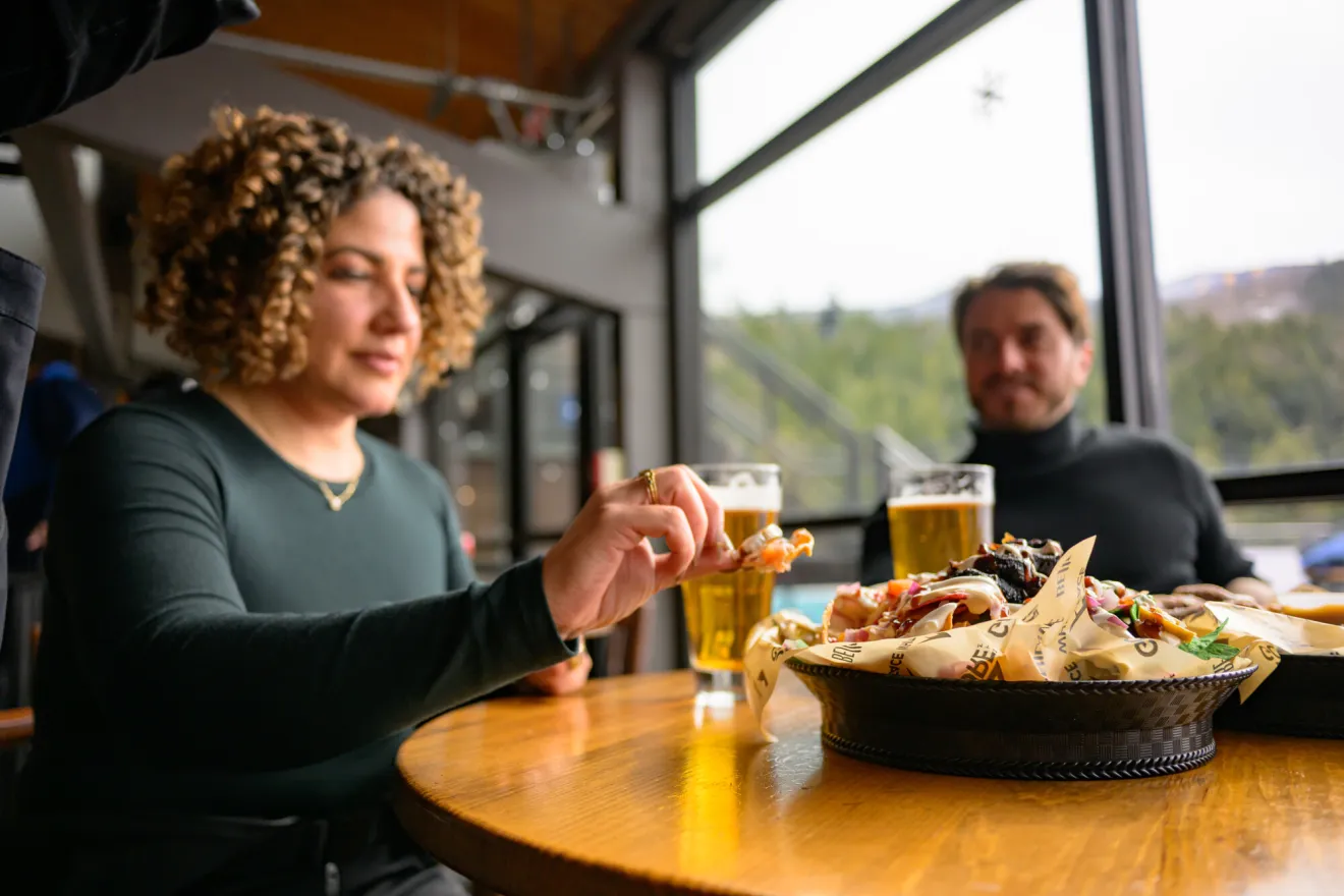 A man and woman enjoy nachos and beer at a mountainside restaurant. 