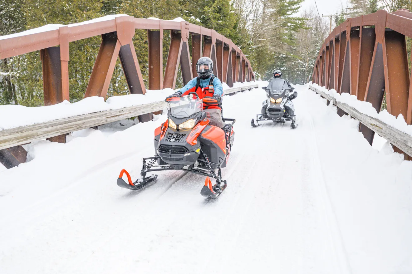 Two snowmobilers riding on a trail.