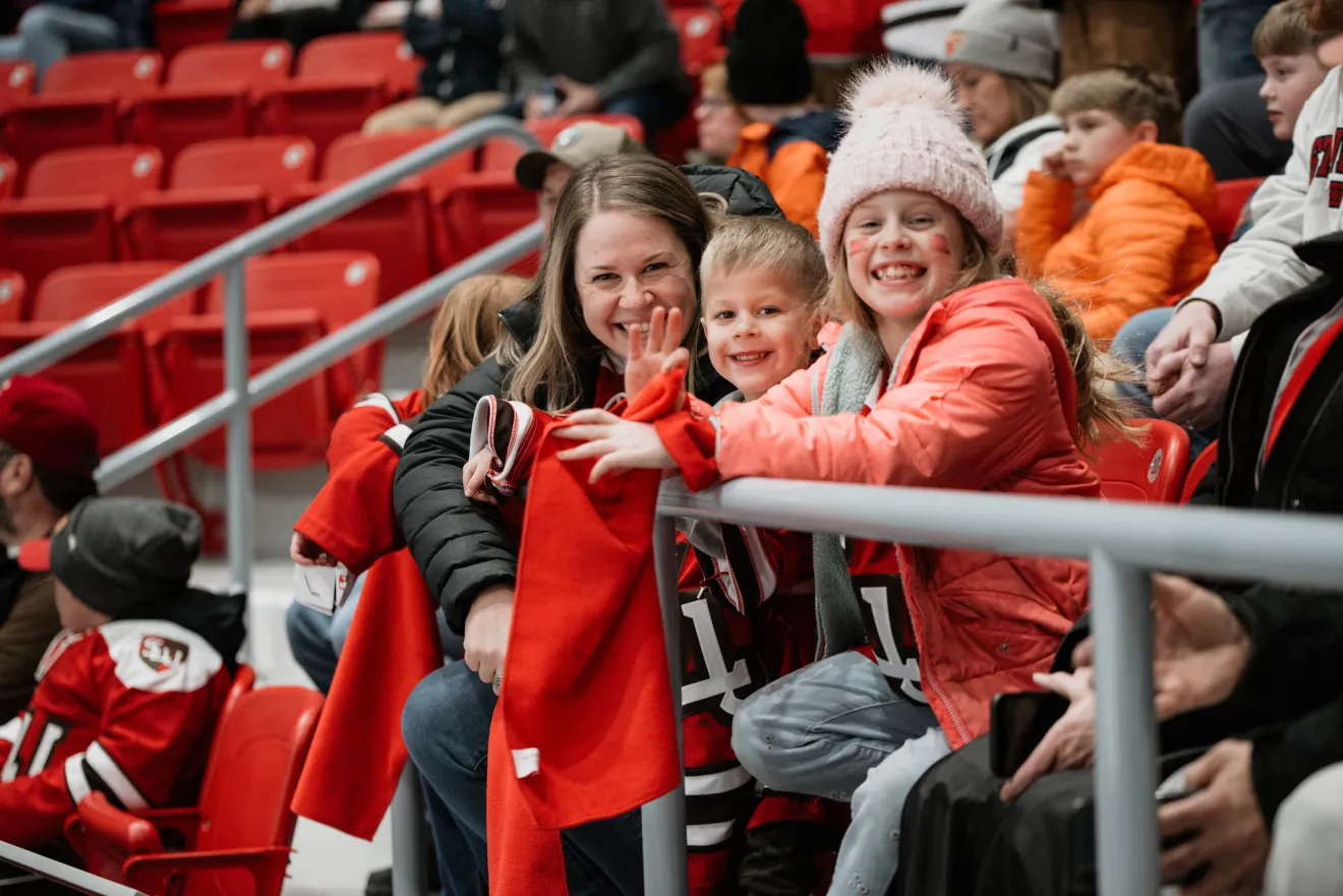 A woman and her two children smile while sitting in stadium seats. 