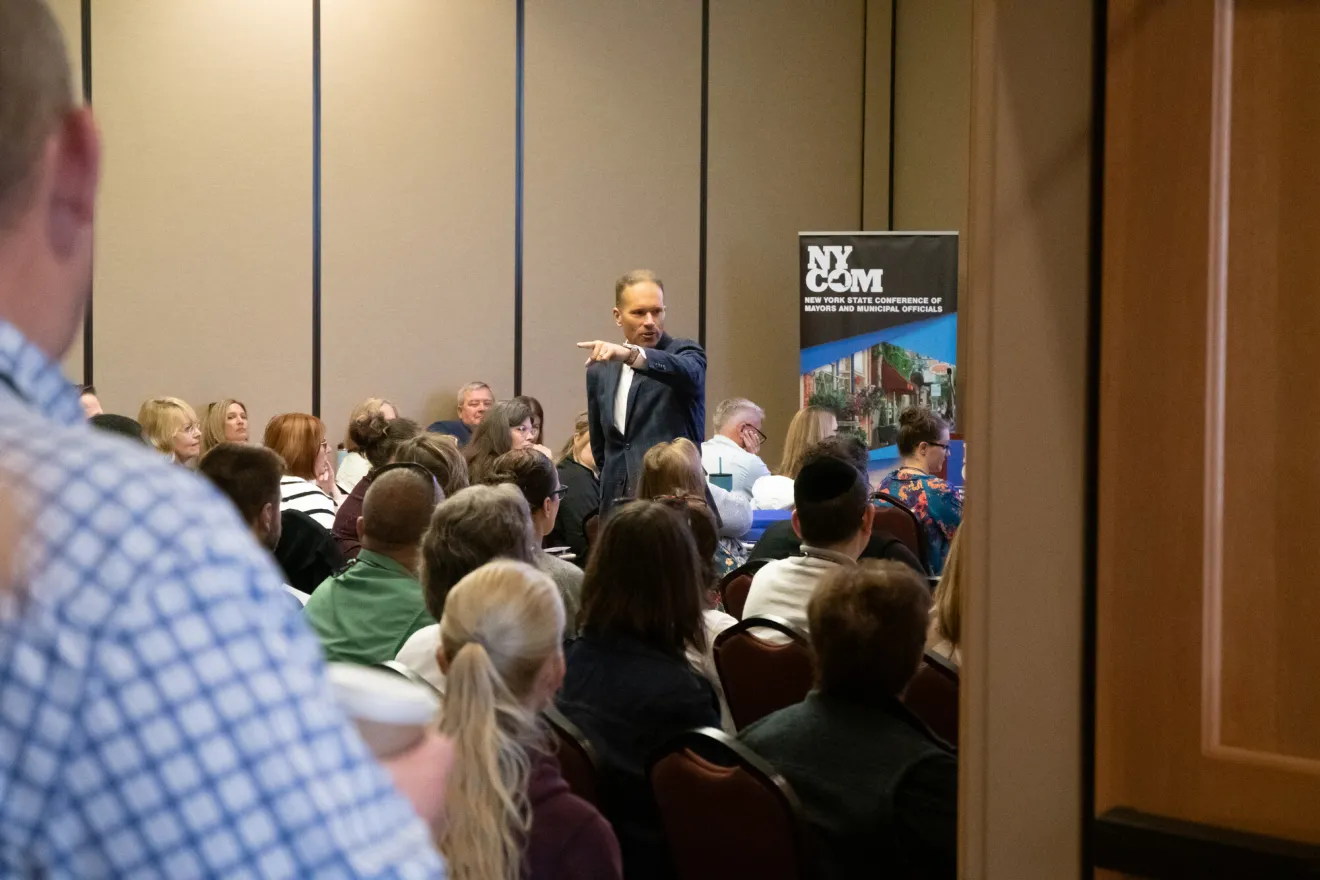 A man in a suit gives a presentation to a room full of people. 
