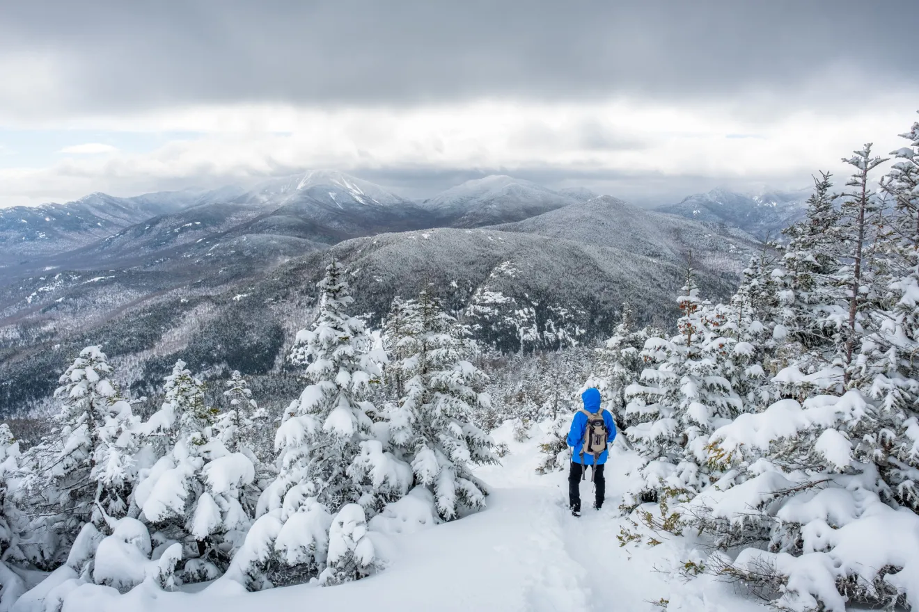 A winter hiker taking in views from a 46 High Peak