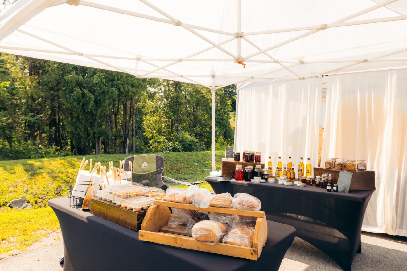A table at a Lake Placid farmers market featuring fresh produce and beverages for sale.