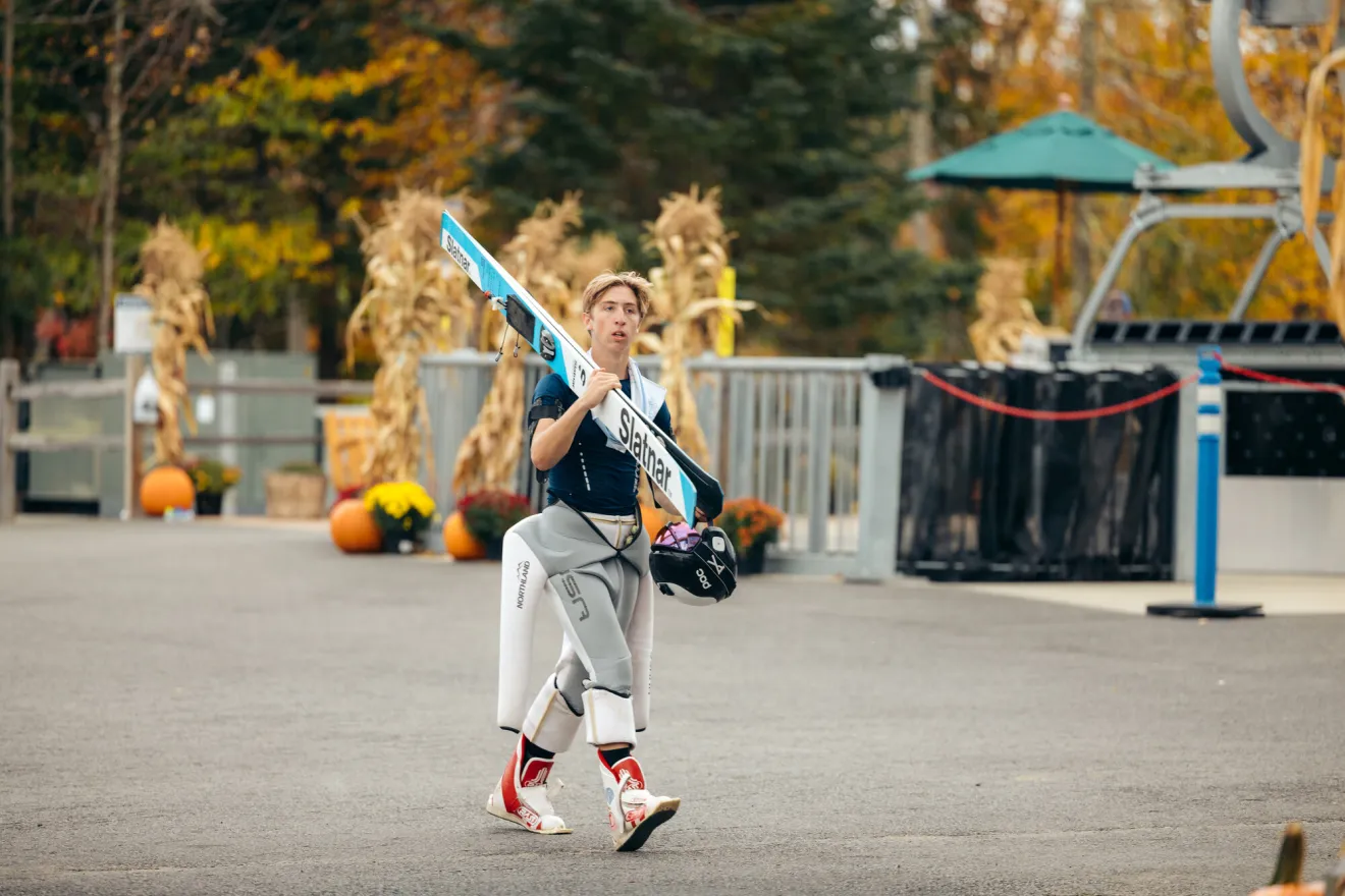 A man carries skis to an event in fall. 