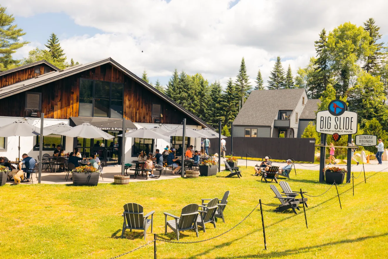 A rustic-themed brewery with a lush green lawn, filled with Adirondack chairs and lawn games. 