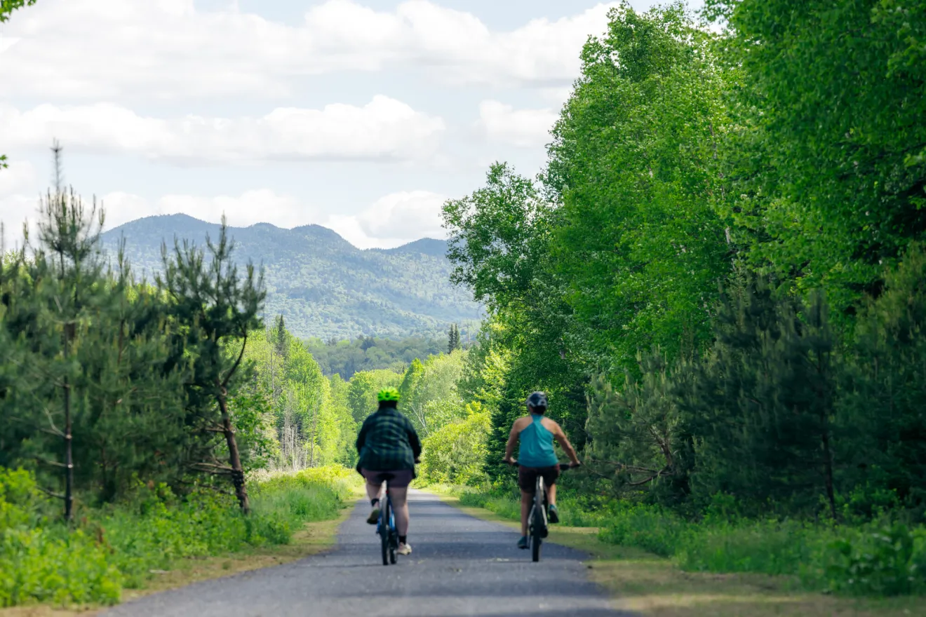 Two women ride bikes on a backcountry road.