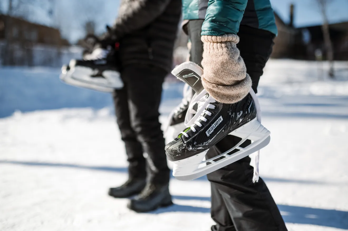 Two people holding their ice skates on a frozen rink.