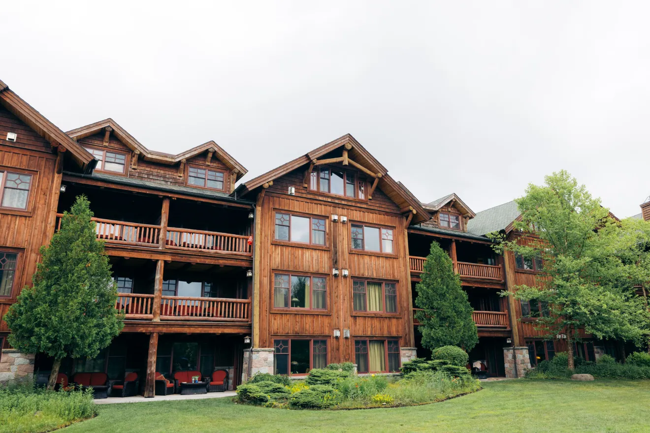 A lodge-style hotel from the outside with greenery and a lawn. 