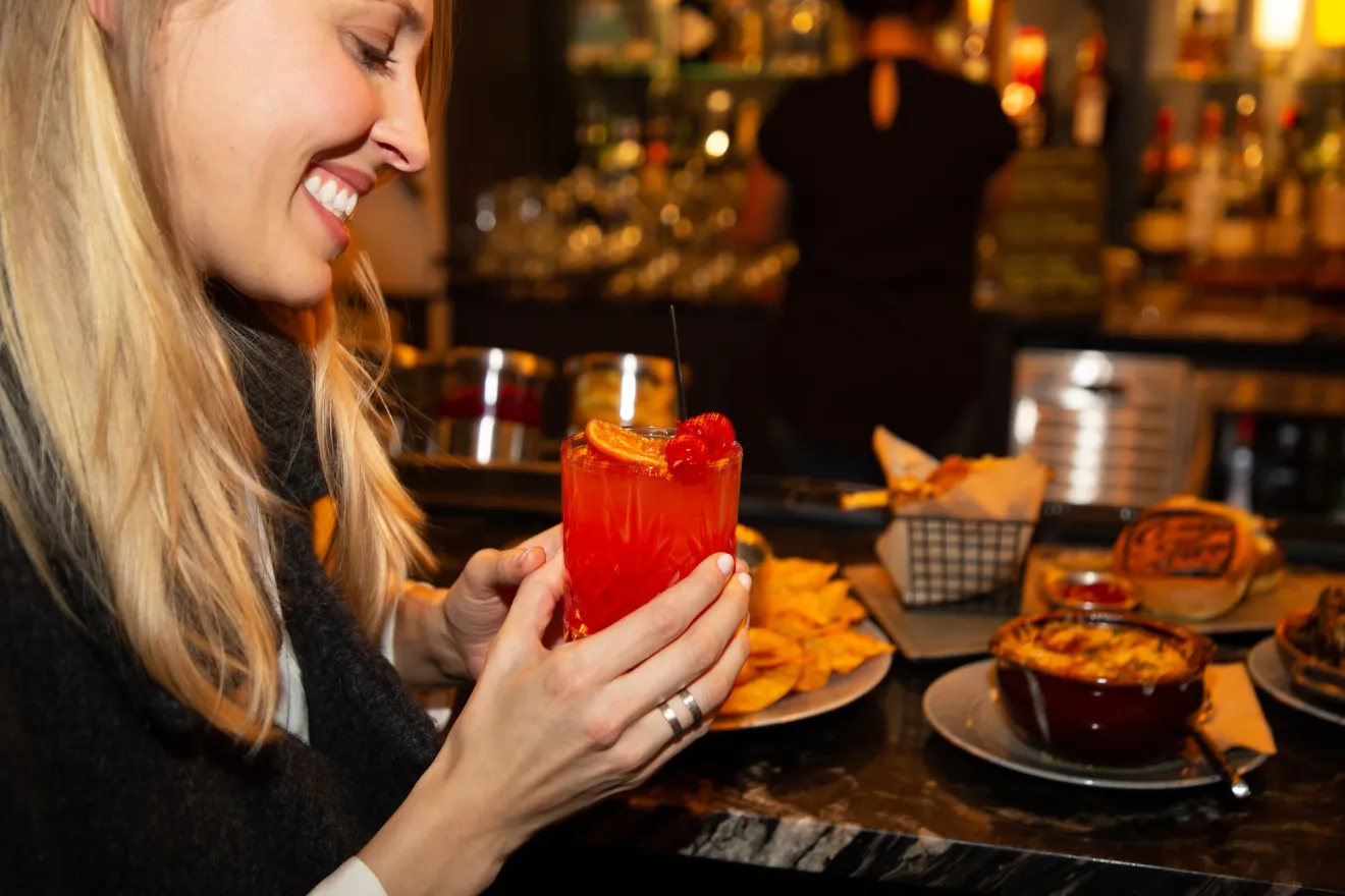 A woman sips a cocktail at a bar. 