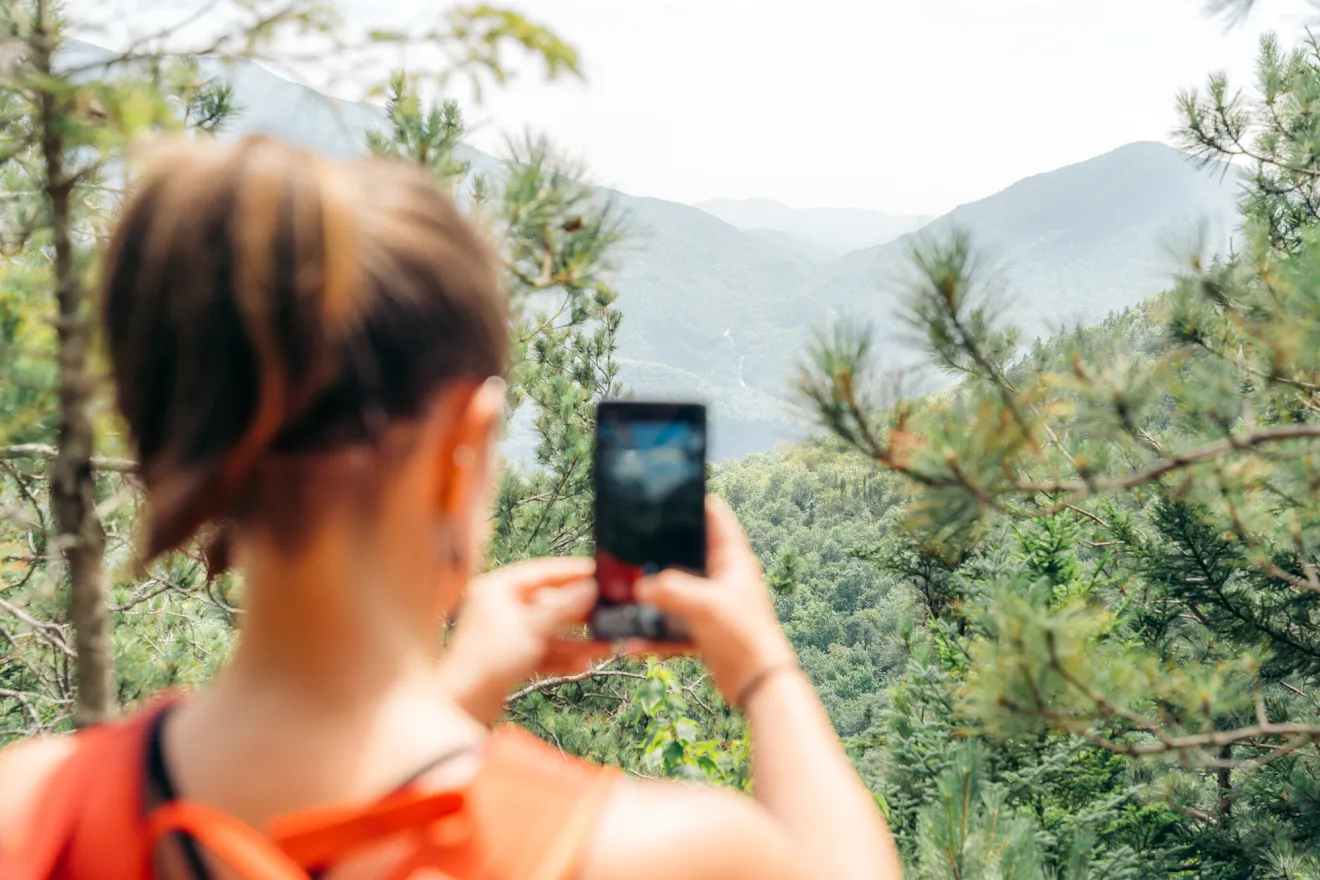 A woman takes a picture of a mountain range. 