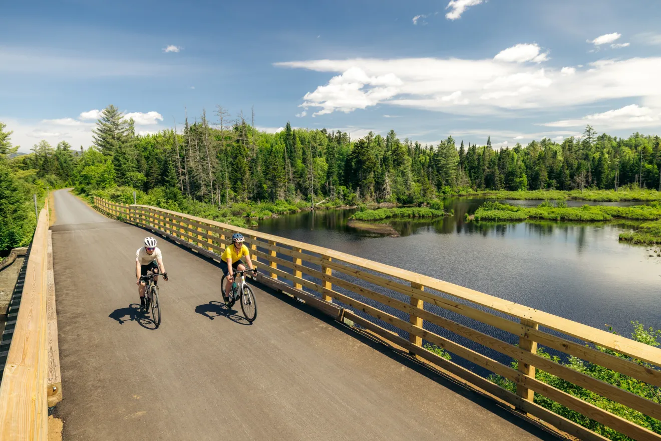 Two people bike on a path over a lake. 