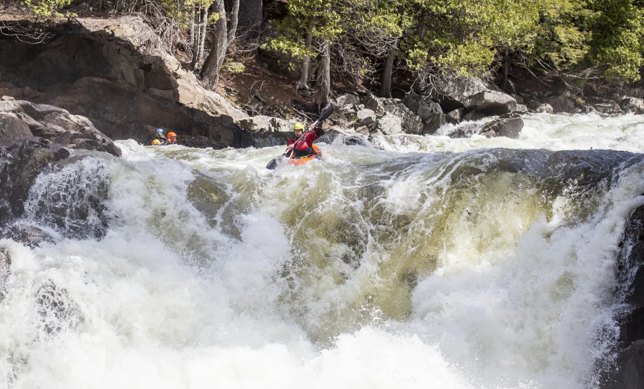 A man dives down a mini water fall on a whitewater route. 