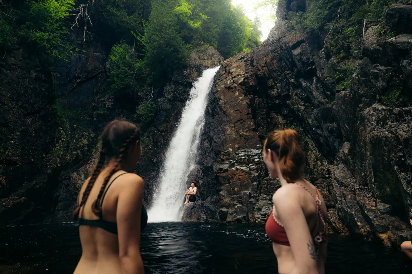 Two women stand in bathing suits at the base of a waterfall. 
