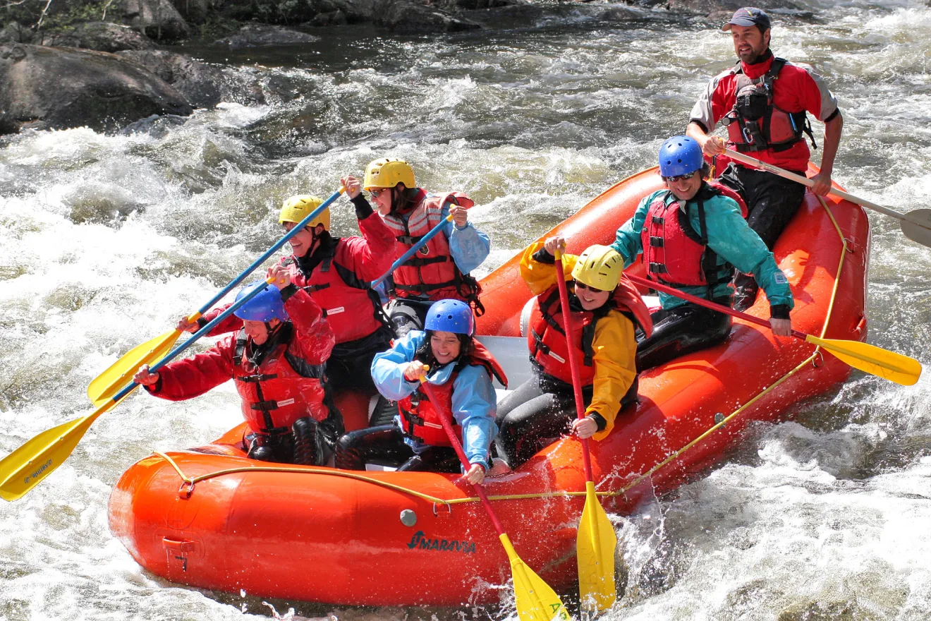 A raft of people paddle down rapids. 