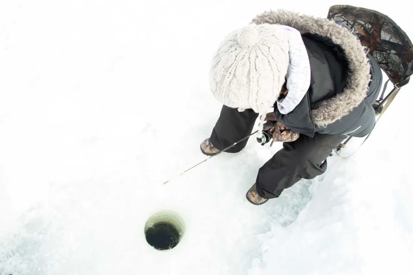 An ice fisher next to a hole