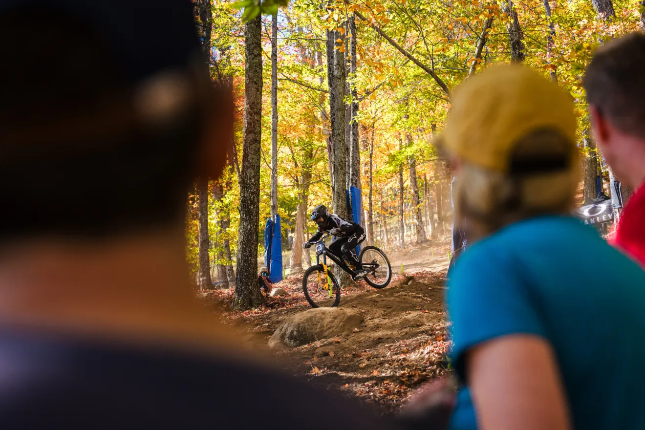 People stand alongside bike course looking on as downhill mountain biker competes in WHOOP UCI MTB Downhill World Cup