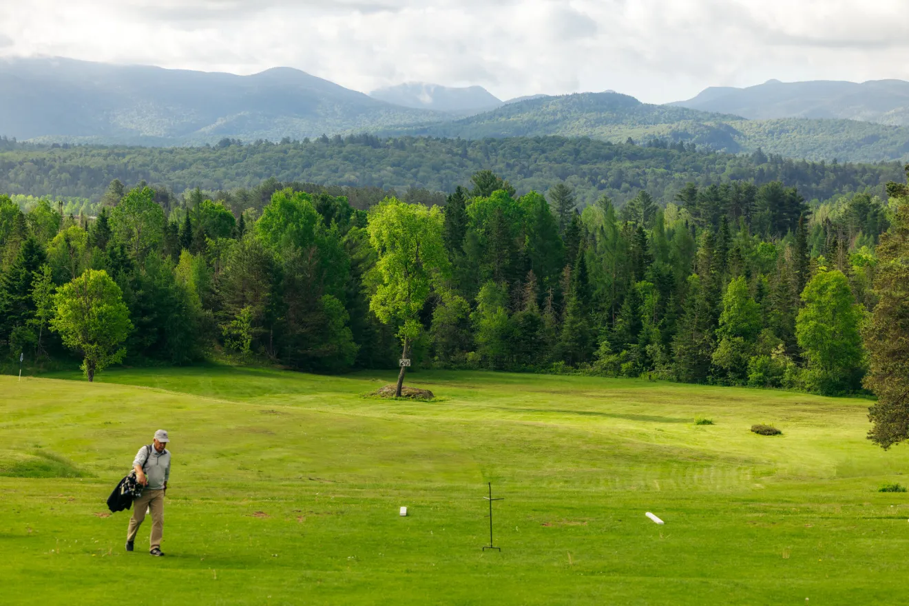 A golfer walking across a Lake Placid golf course