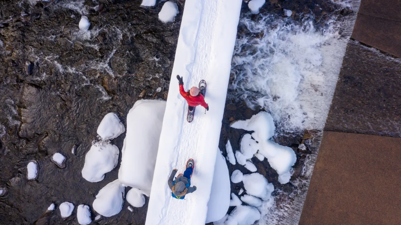 An overhead view of two people crossing a bridge in winter. 