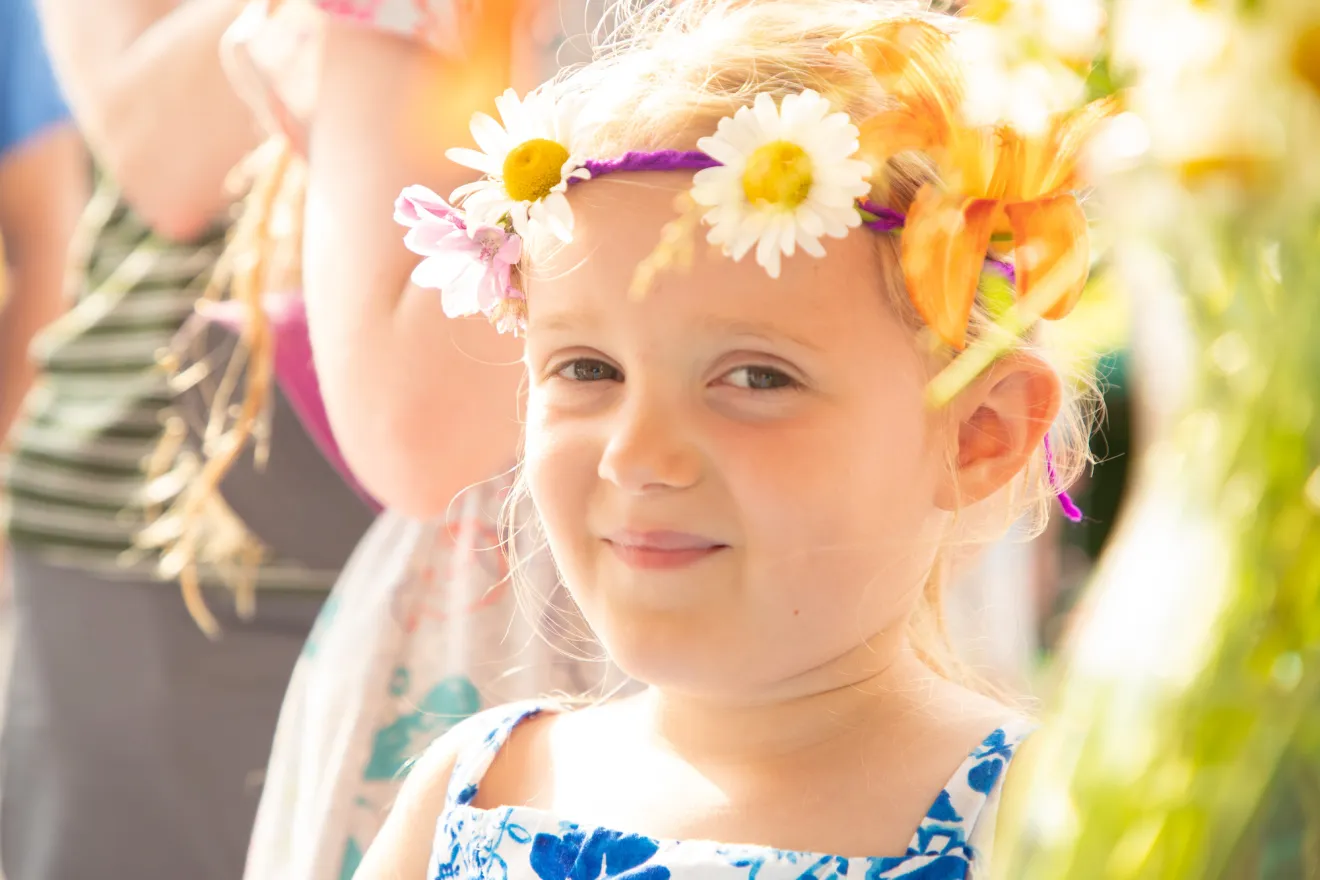 A little girl smiles looking at the camera with flowers in her hair. 