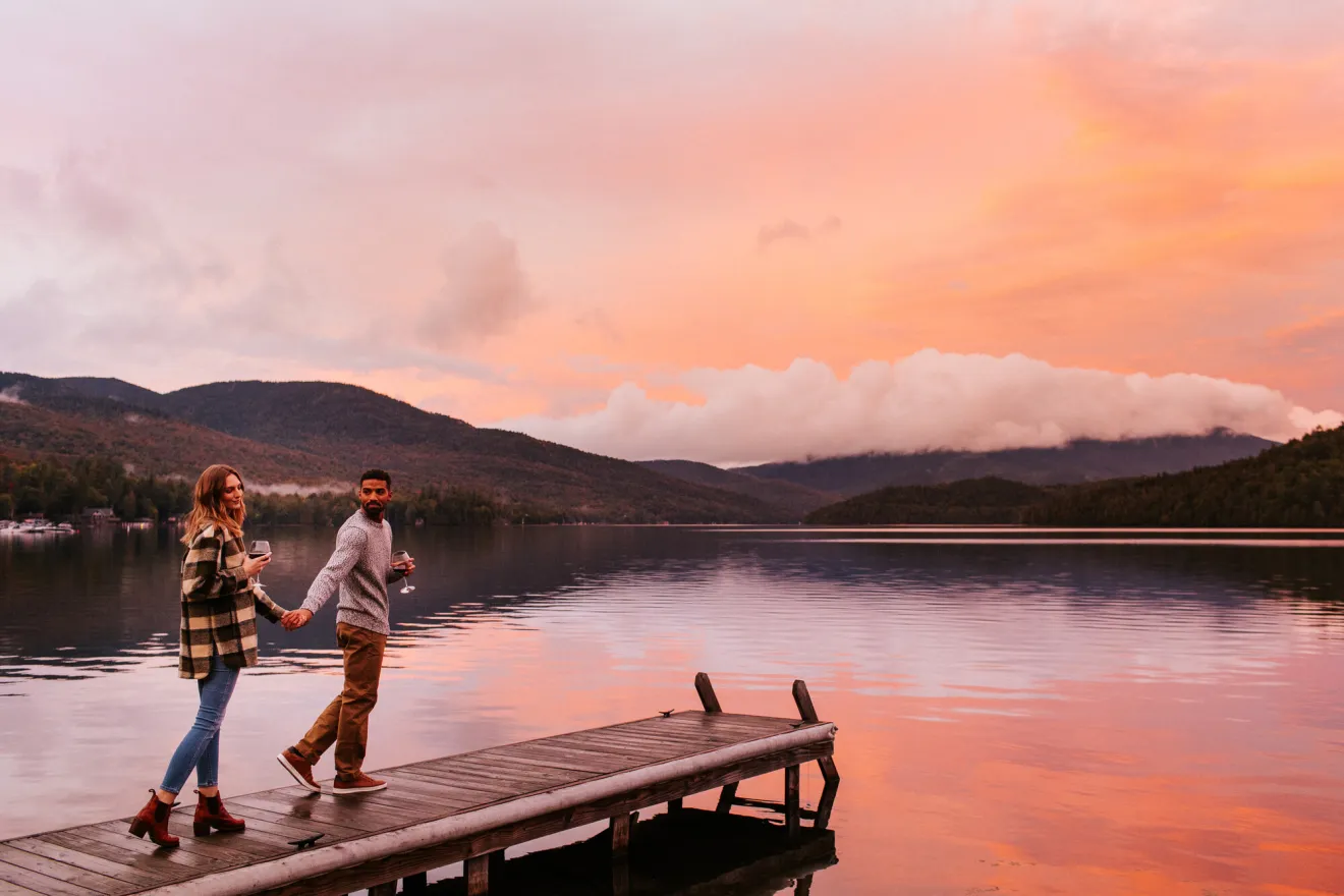 A man and woman walk out onto a dock at sunset. 