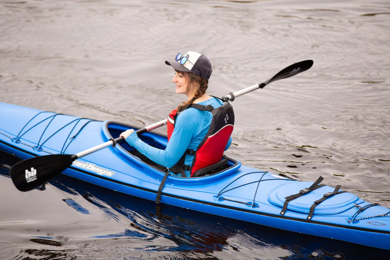 A woman paddles in a blue kayak. 