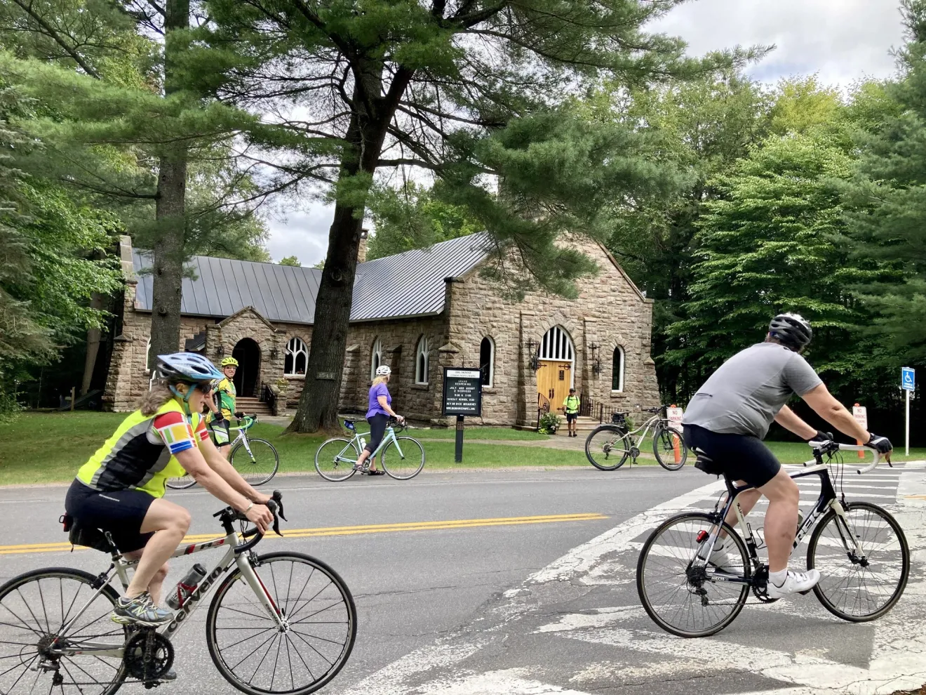 A group of cyclists ride by a church.