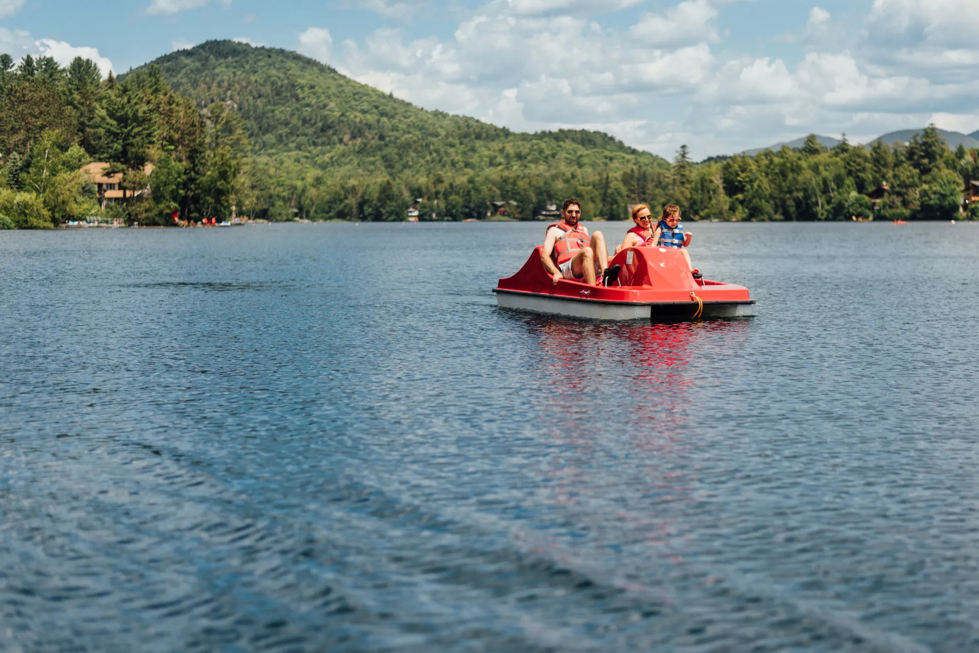 Parents and young child in red peddle boat on lake with mountain in background