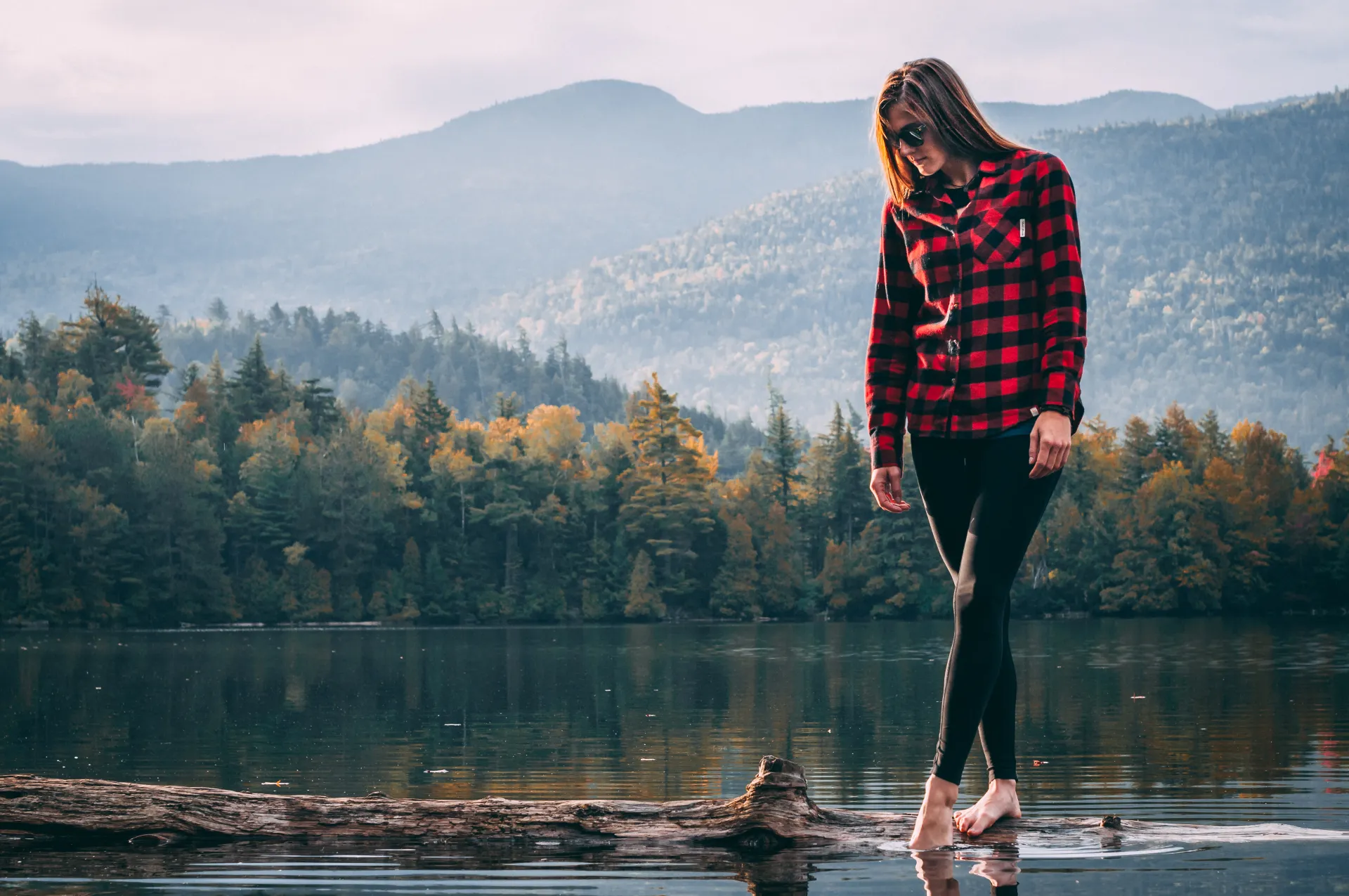 A woman walks on a log in a pond