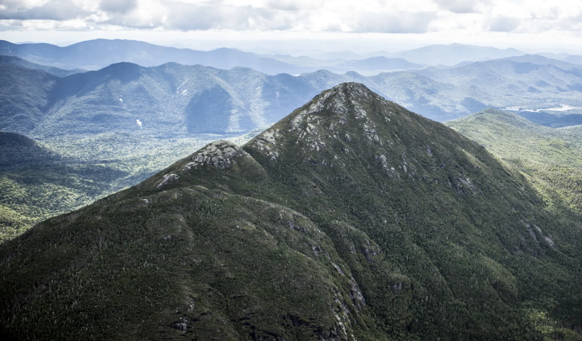 An aerial view of the towering High Peaks, with rocky summits and forested slopes.