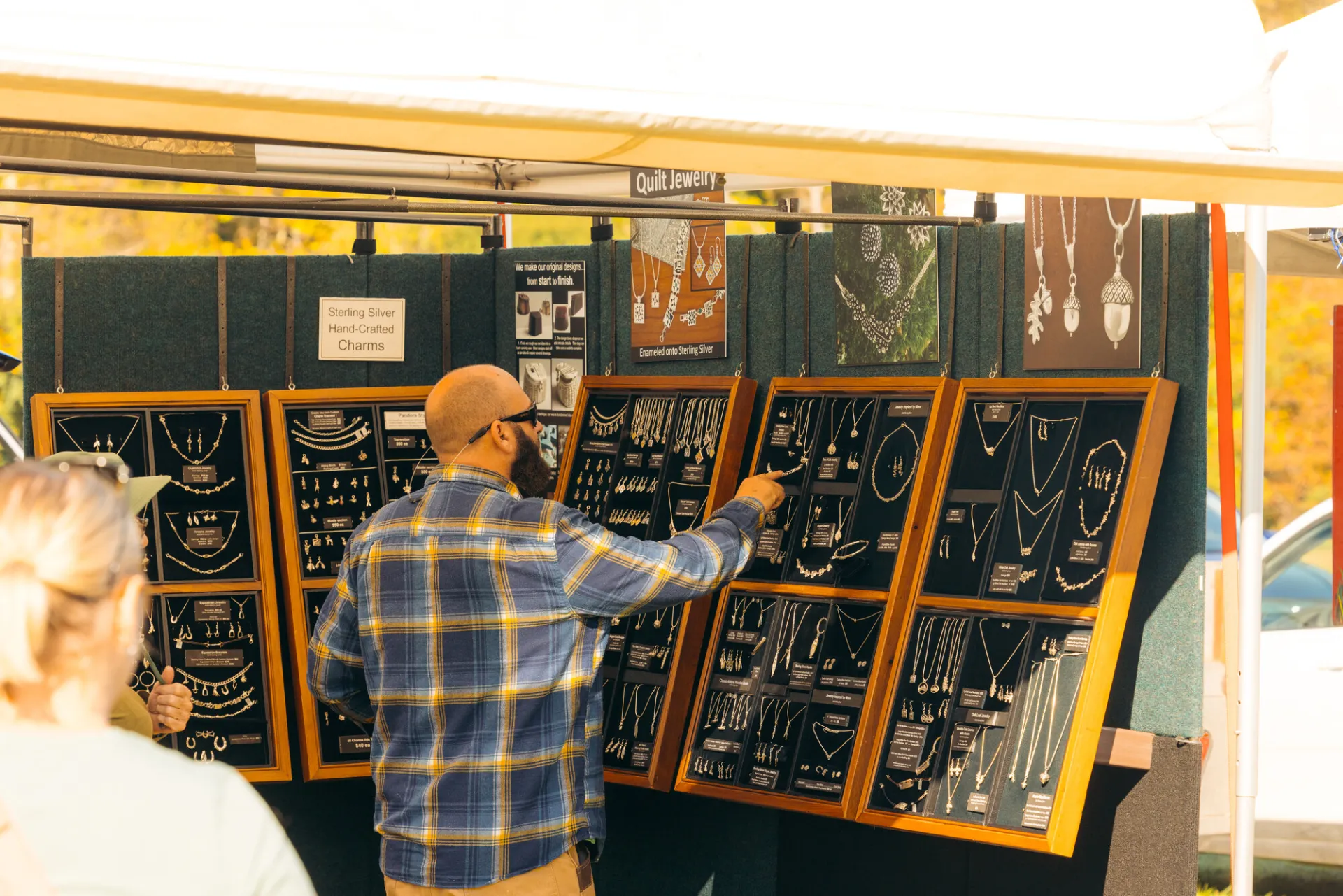 Man wearing flannel and hat browses displays of silver jewelry in farmers market booth