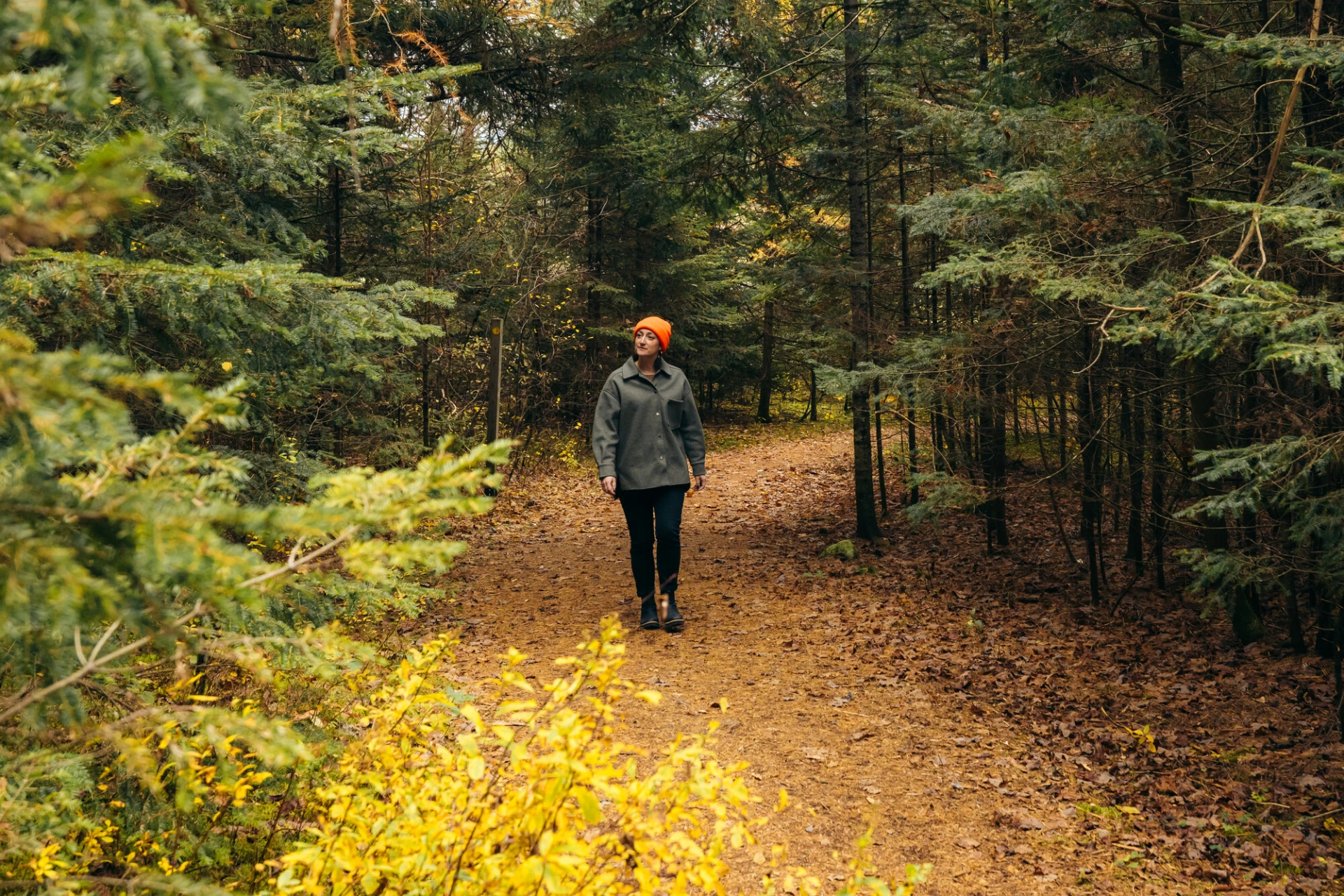 A woman standing on a trail during the fall with a bright orange hat on.