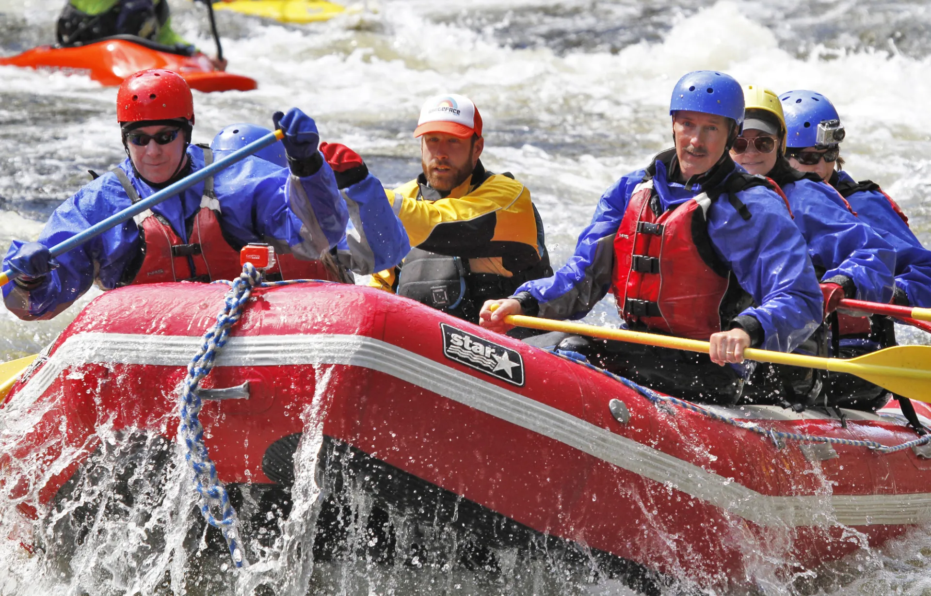 A group of people wear rafting gear and paddle through rapids.