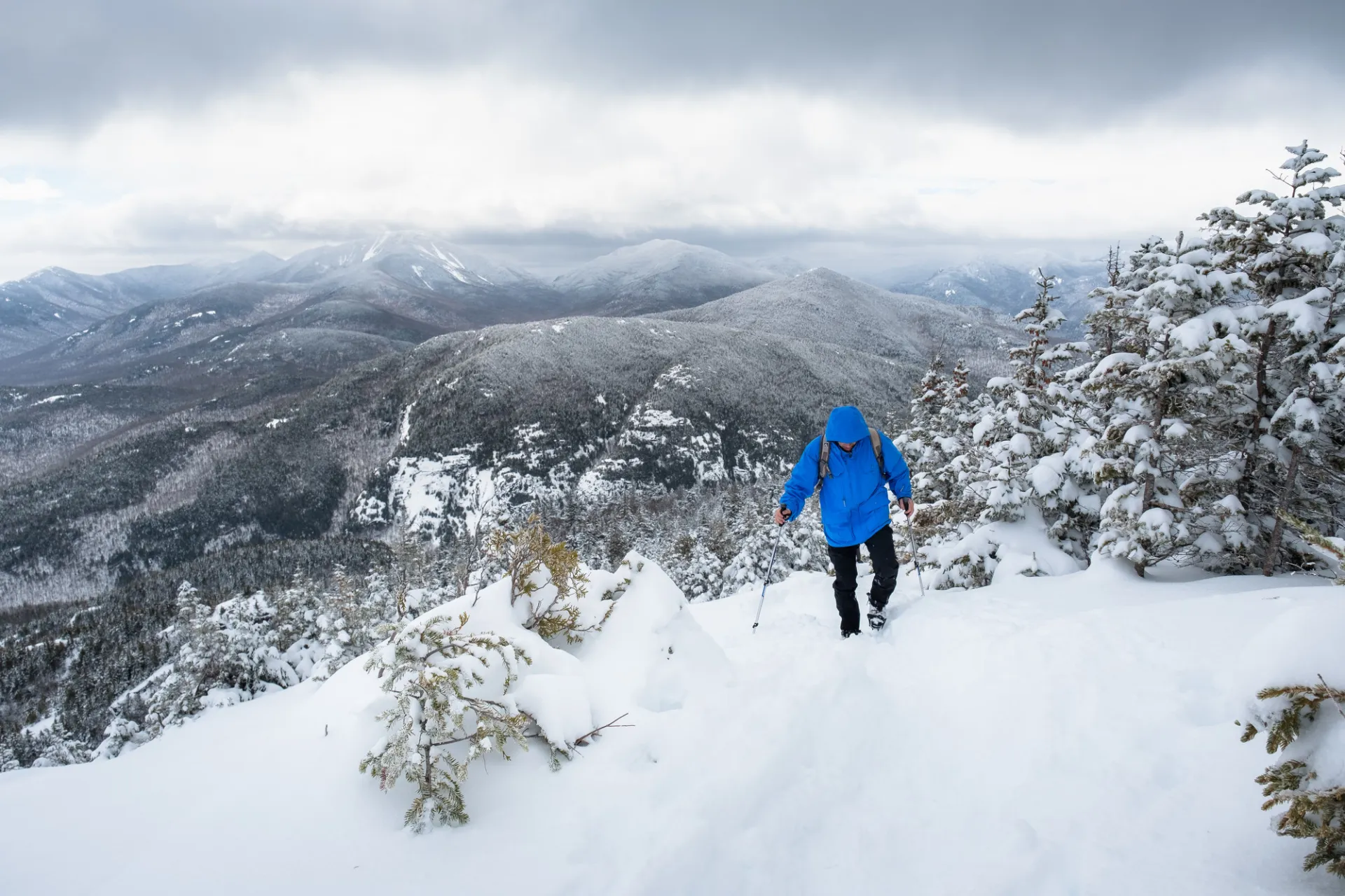 A man in a blue coat walks up a snowy mountain trail
