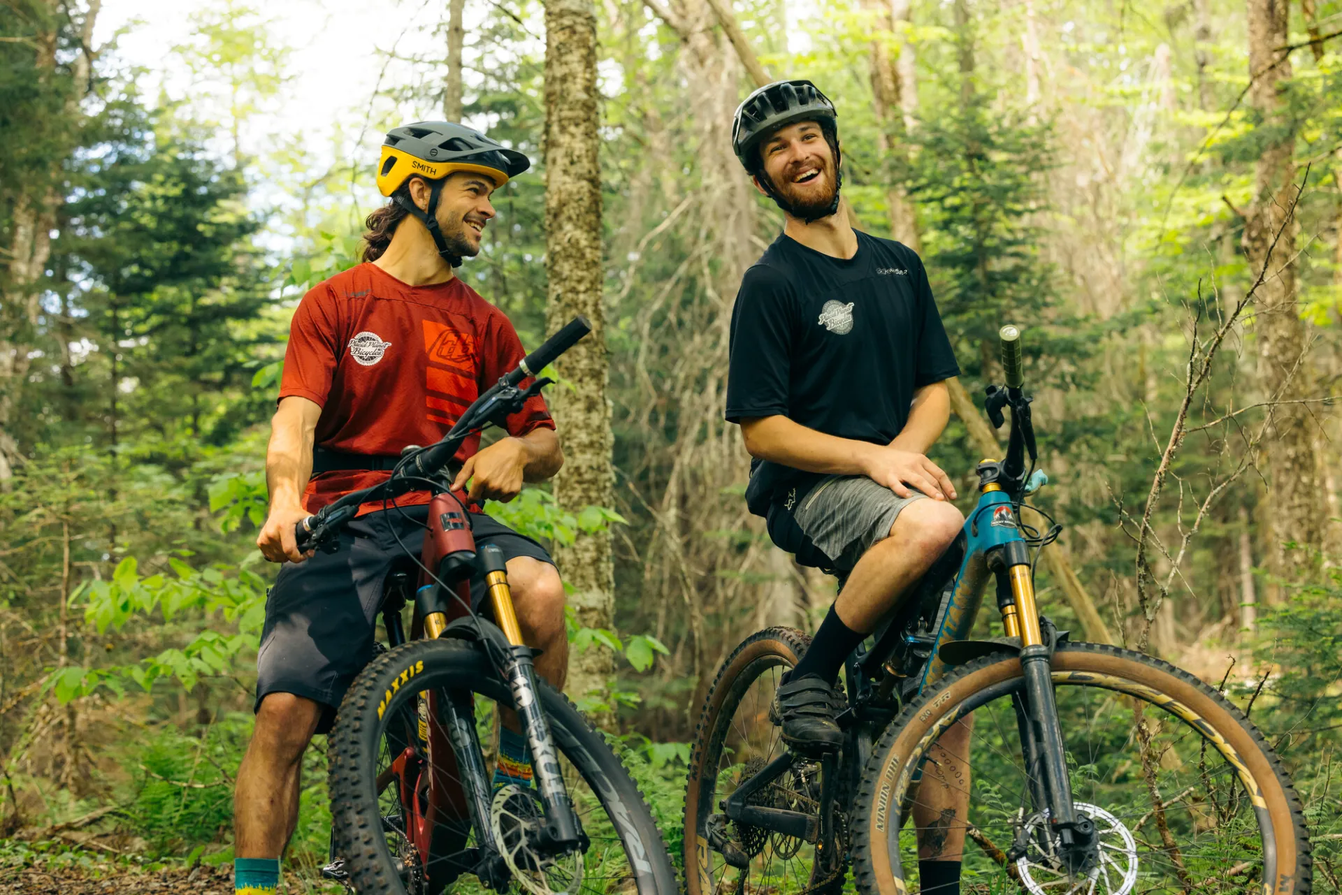 Two bikers on a trail standing and laughing together.