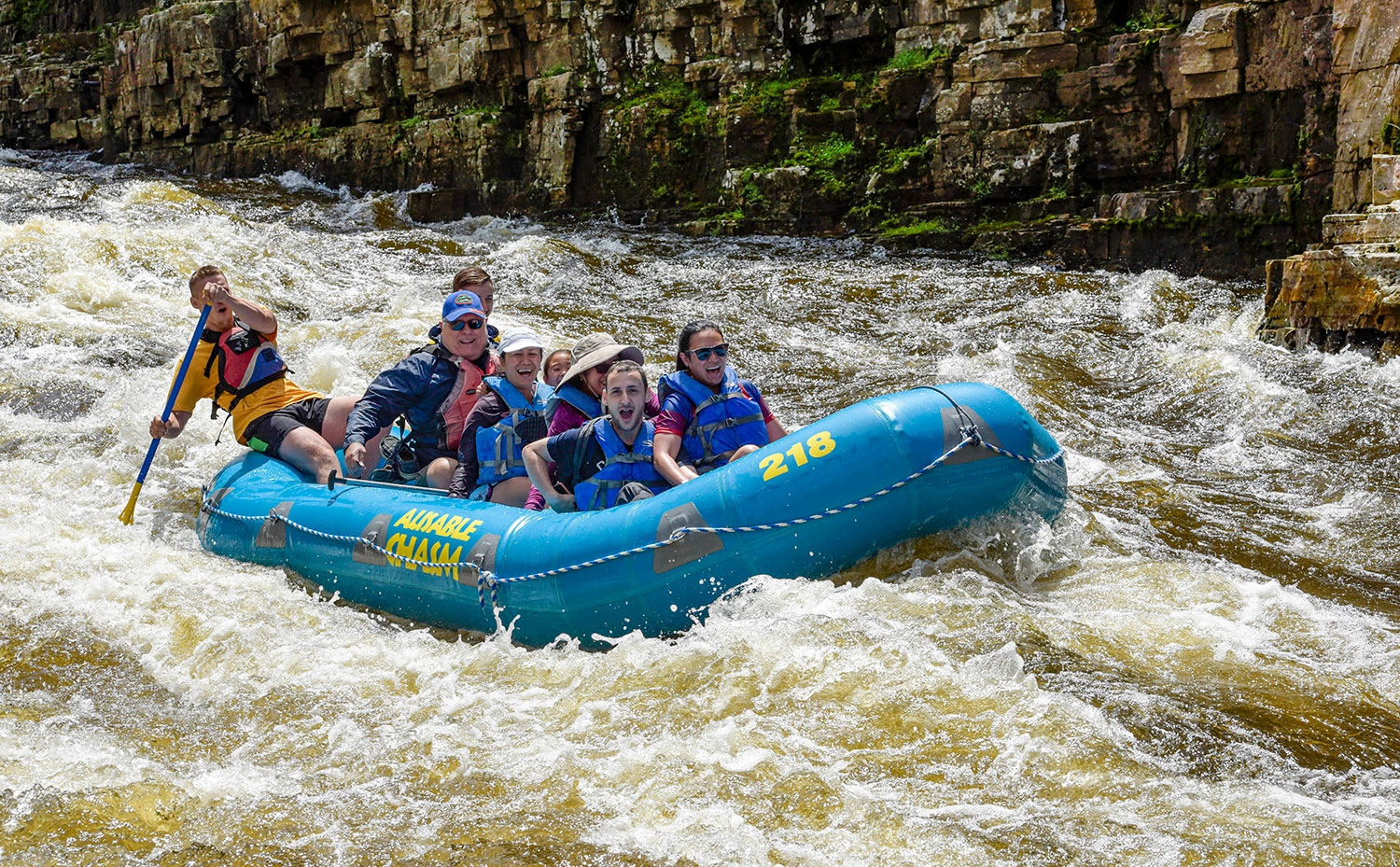A happy group of people ride a blue raft through the Au Sable Chasm.