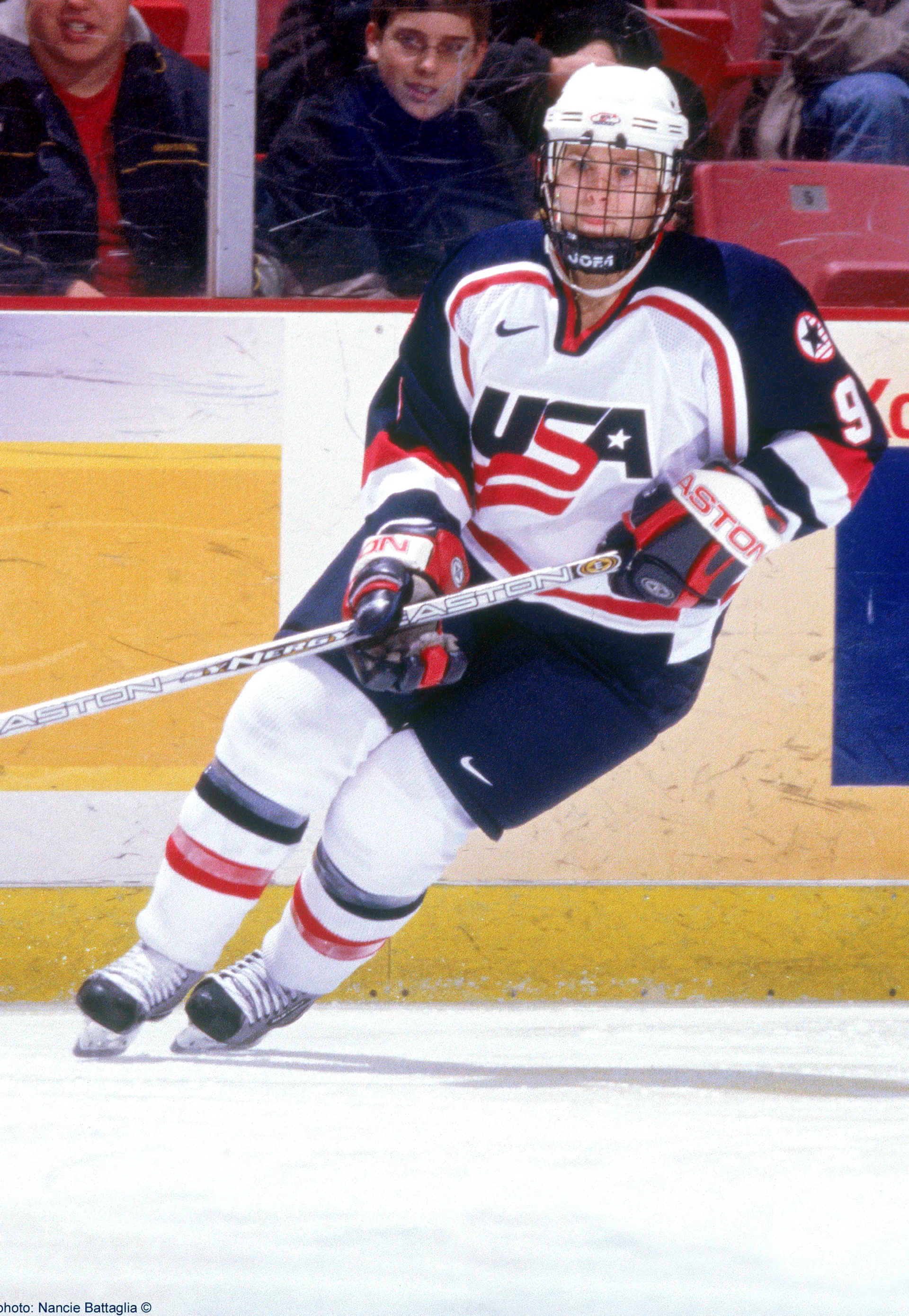 A female hockey player wearing a team USA jersey skates on a competition hockey rink.