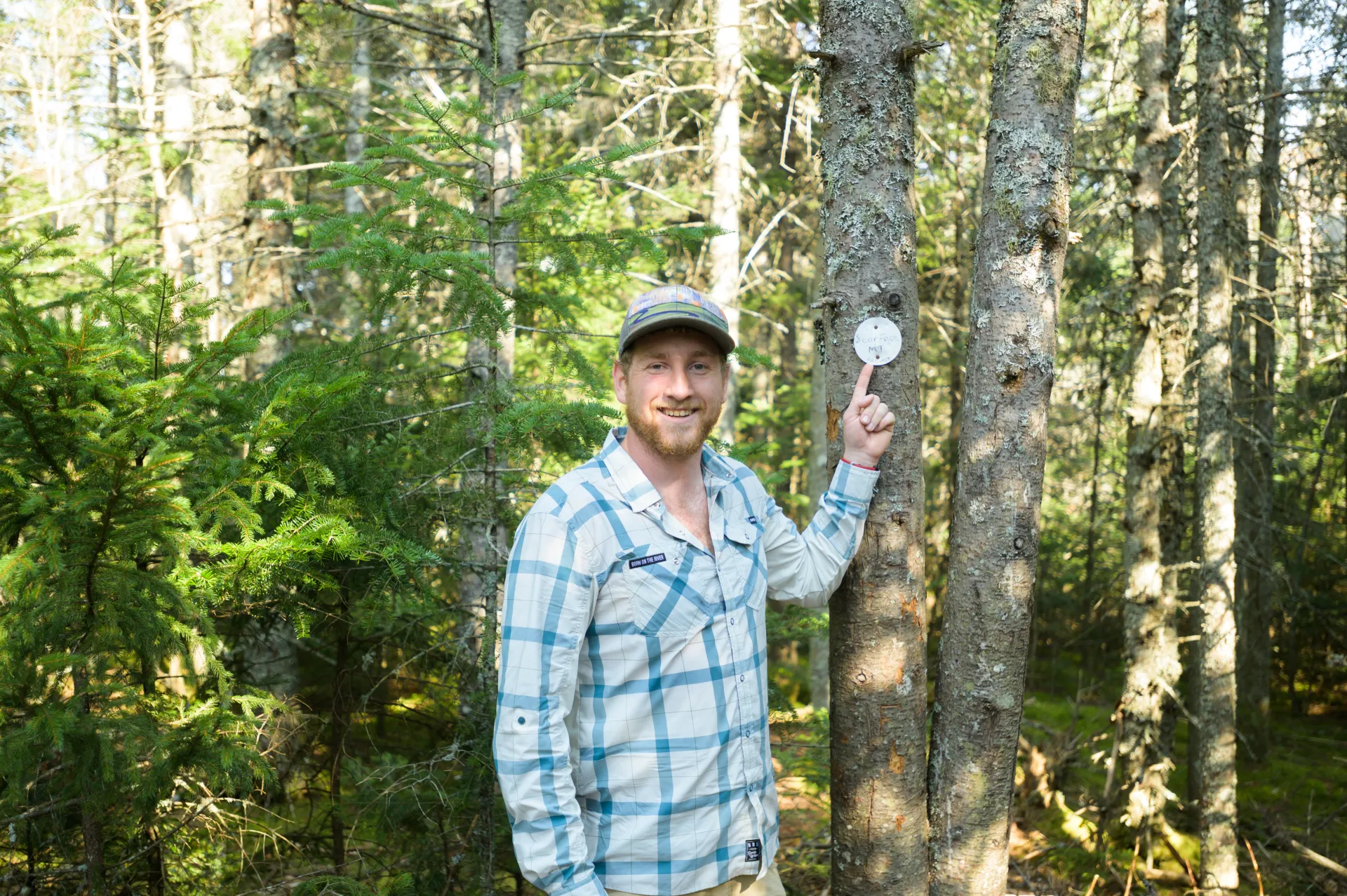 A hiker points to a marker on the top of a mountain