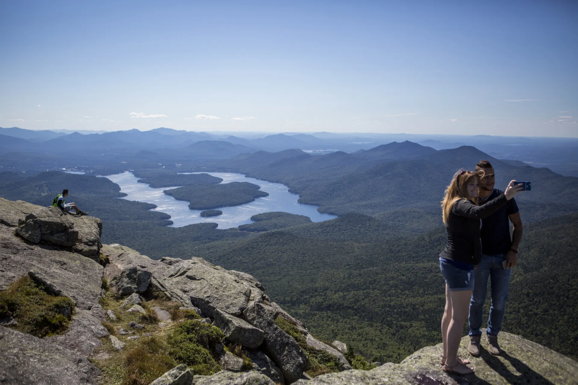 Two adults take a "selfie" on a rock high above a forest and lake.