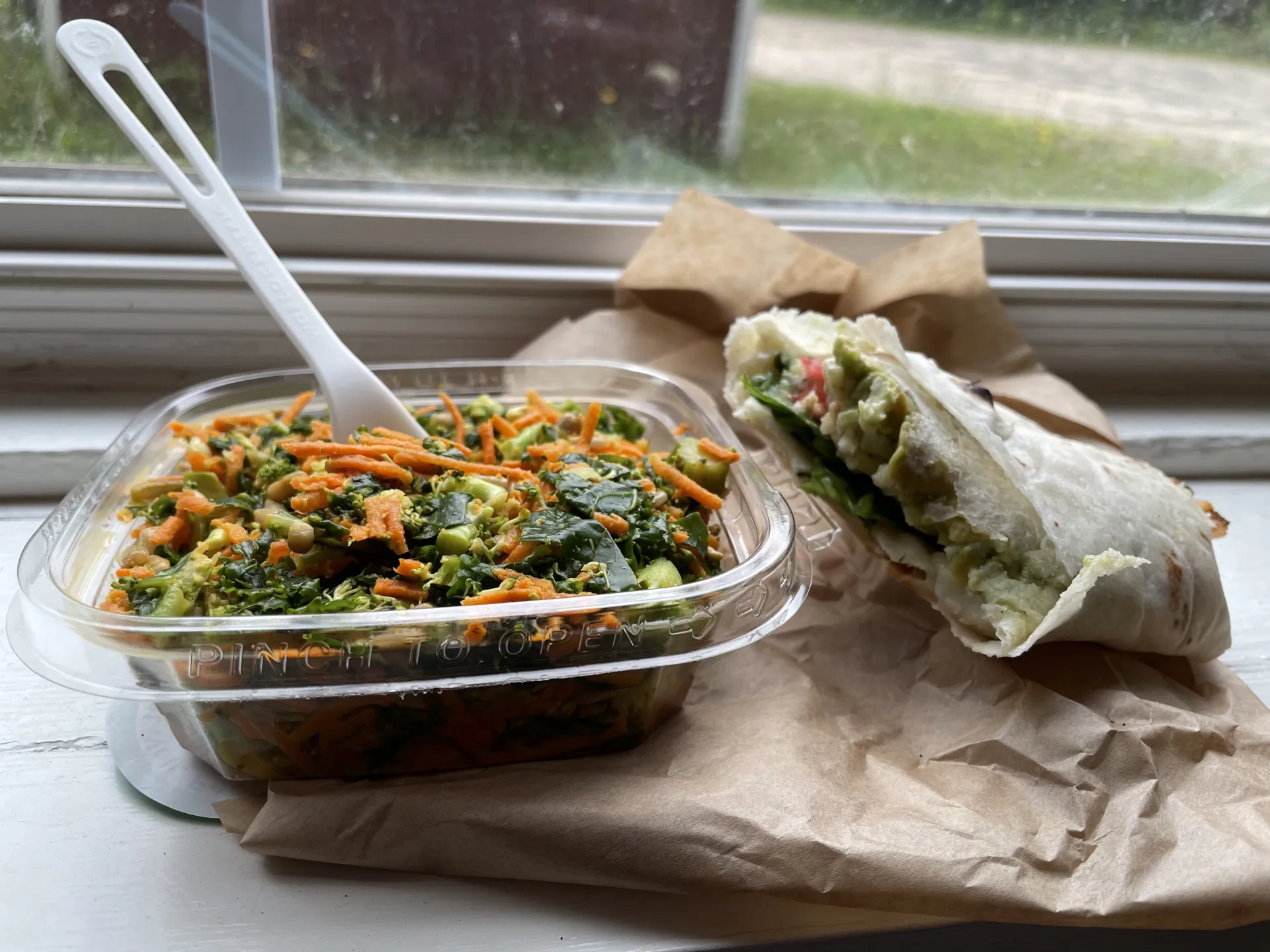 A gluten-free and vegan to-go meal of a kale/carrot salad and wrap with avocado and spinach.
