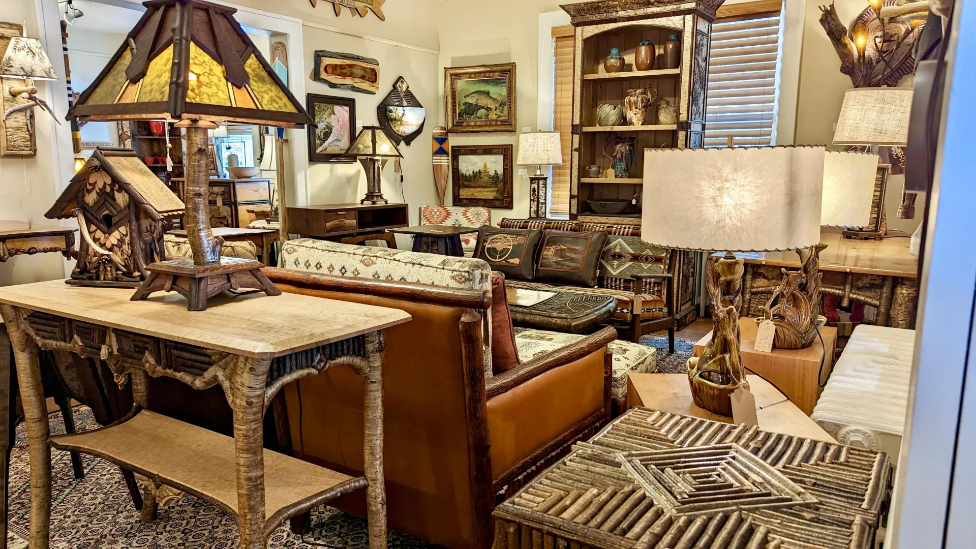 A view of the show room at L Post Rustics featuring many styles of log furniture from end table to couches, table lamps, sconces and tall hutches flanked by wall decor.