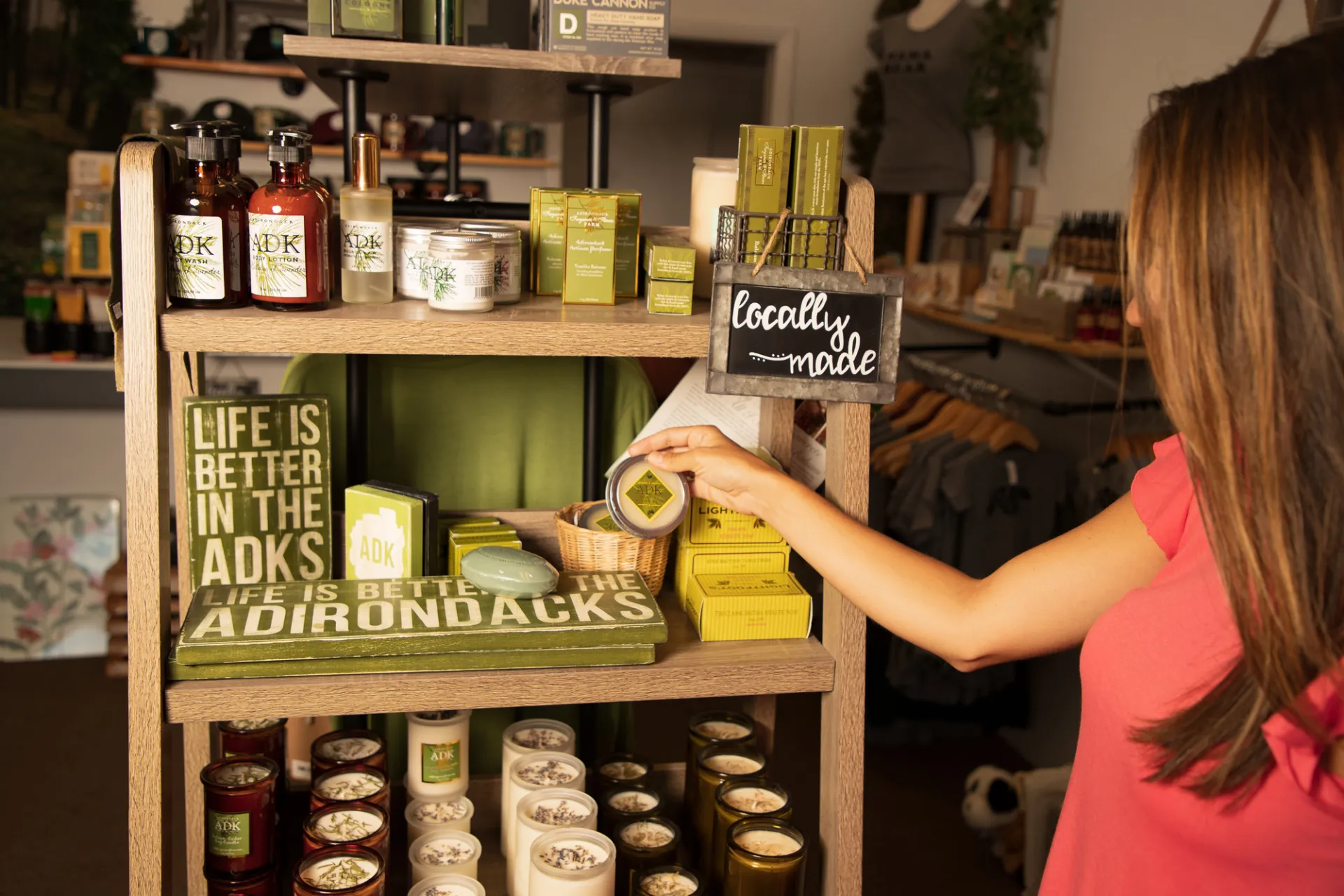 A woman reaches for a container on a wooden shelf stocked with locally made Adirondack-themed soaps, lotions, and candles.