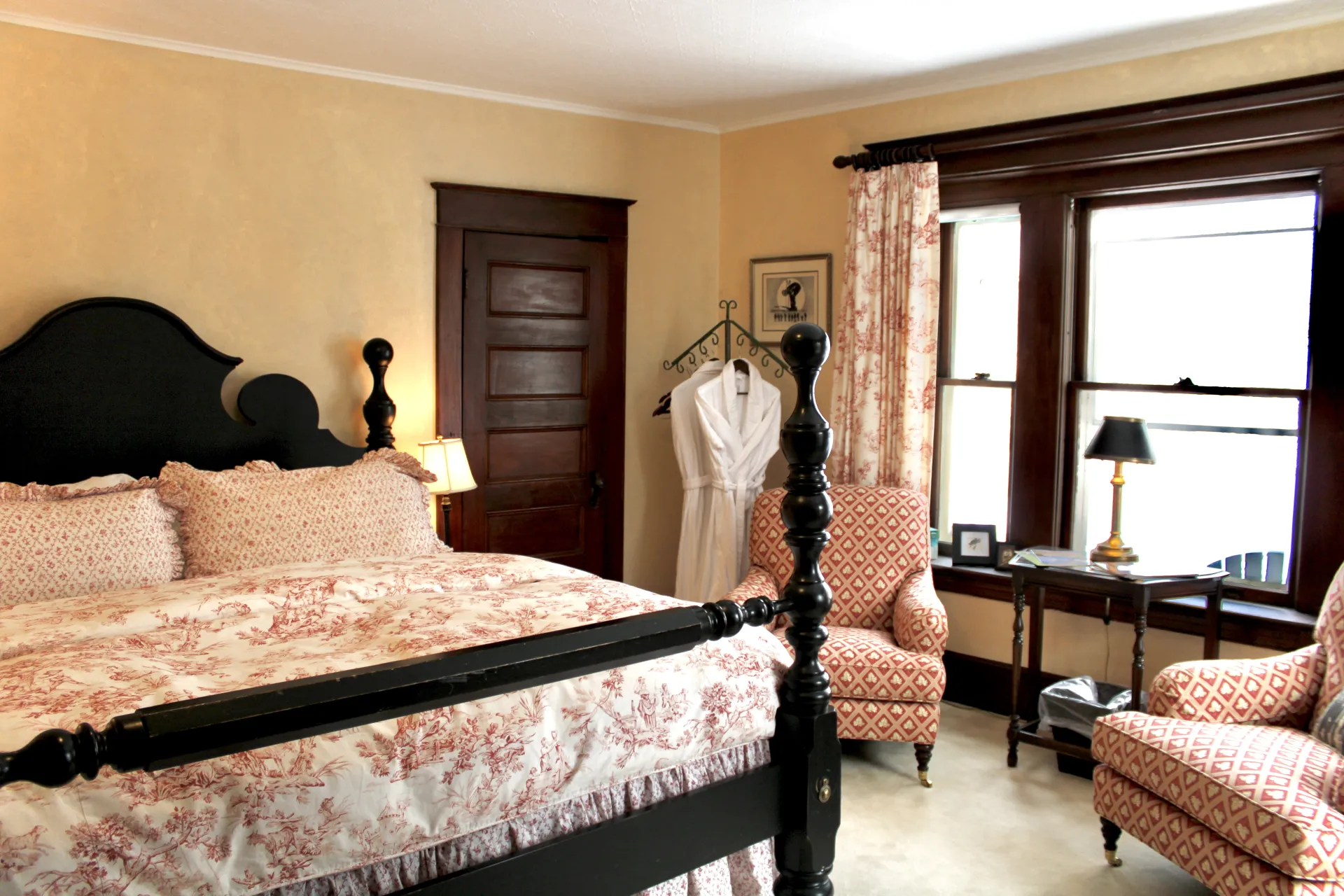 Dark furniture in a large bedroom with pink chair.