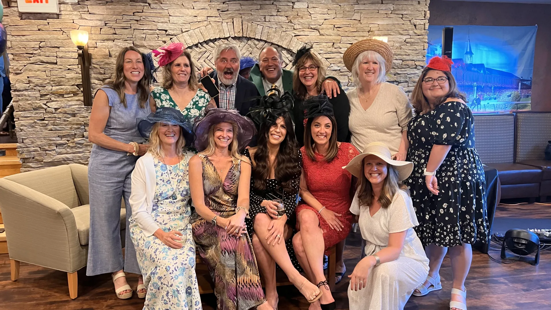 Large group of people in Derby dress pose for group photo in front of stone wall in restaurant