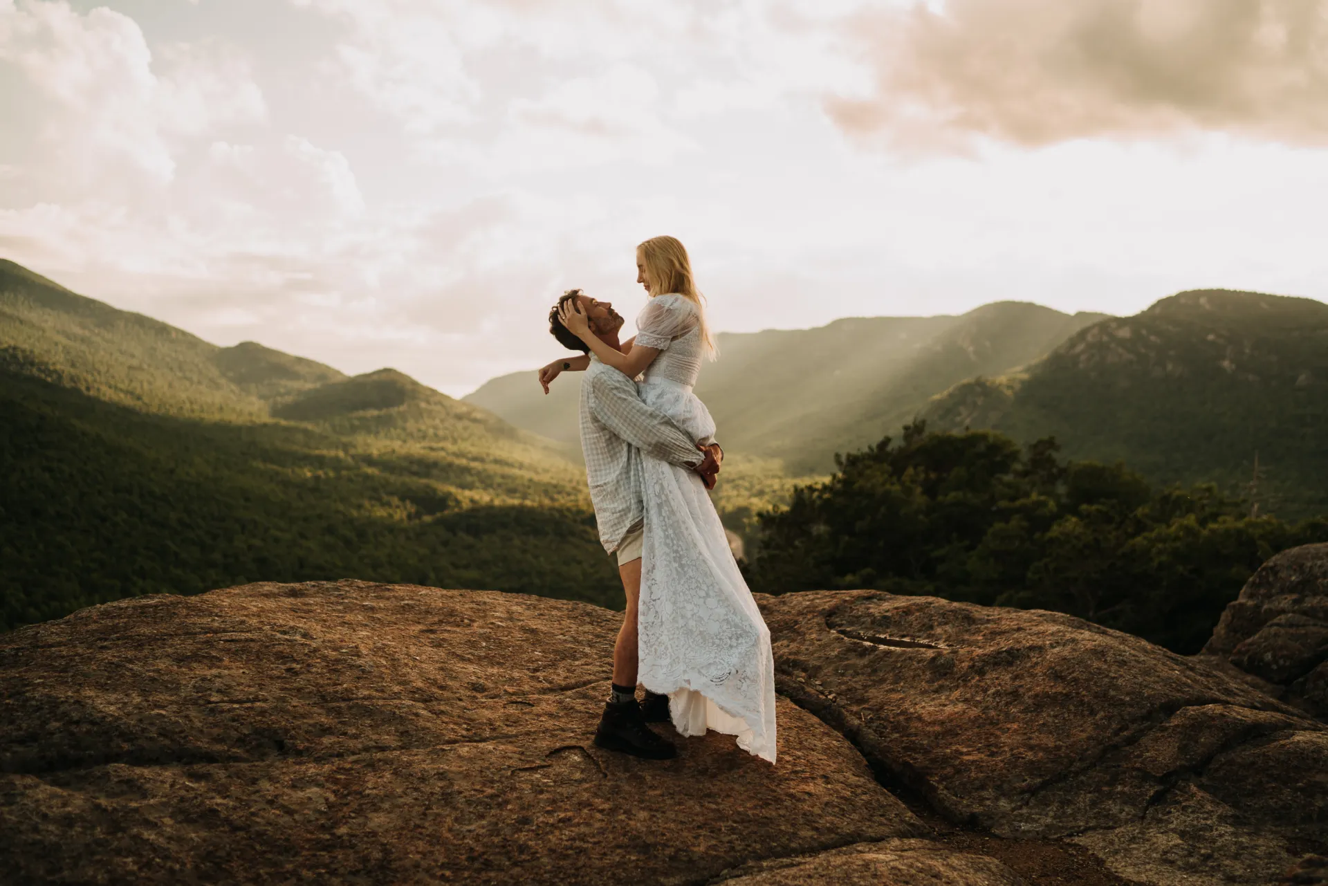 man holds his wife up on top of a mountain