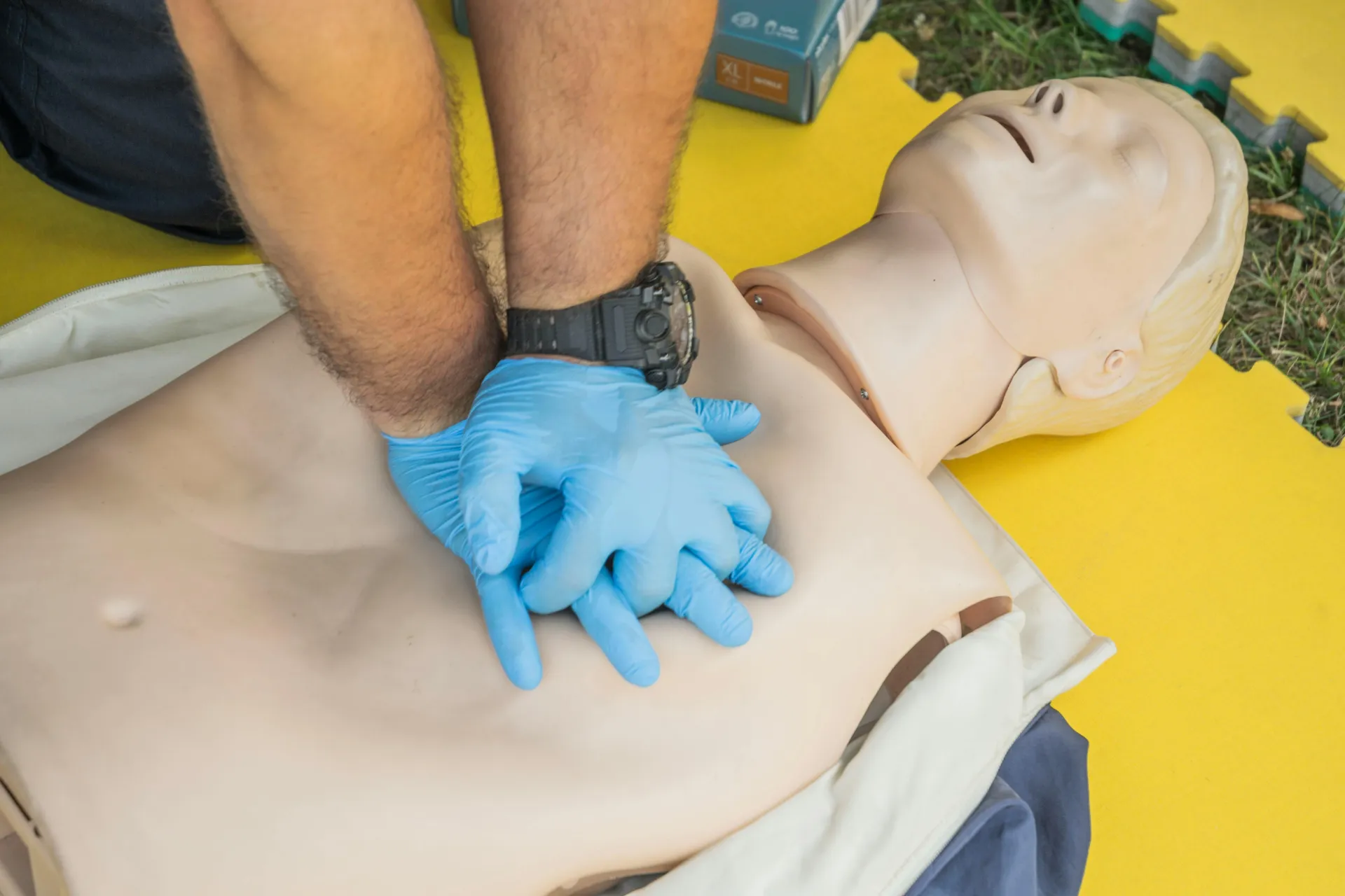 Person's hands in blue medical gloves and arms seen practicing CPR compressions on dummy doll