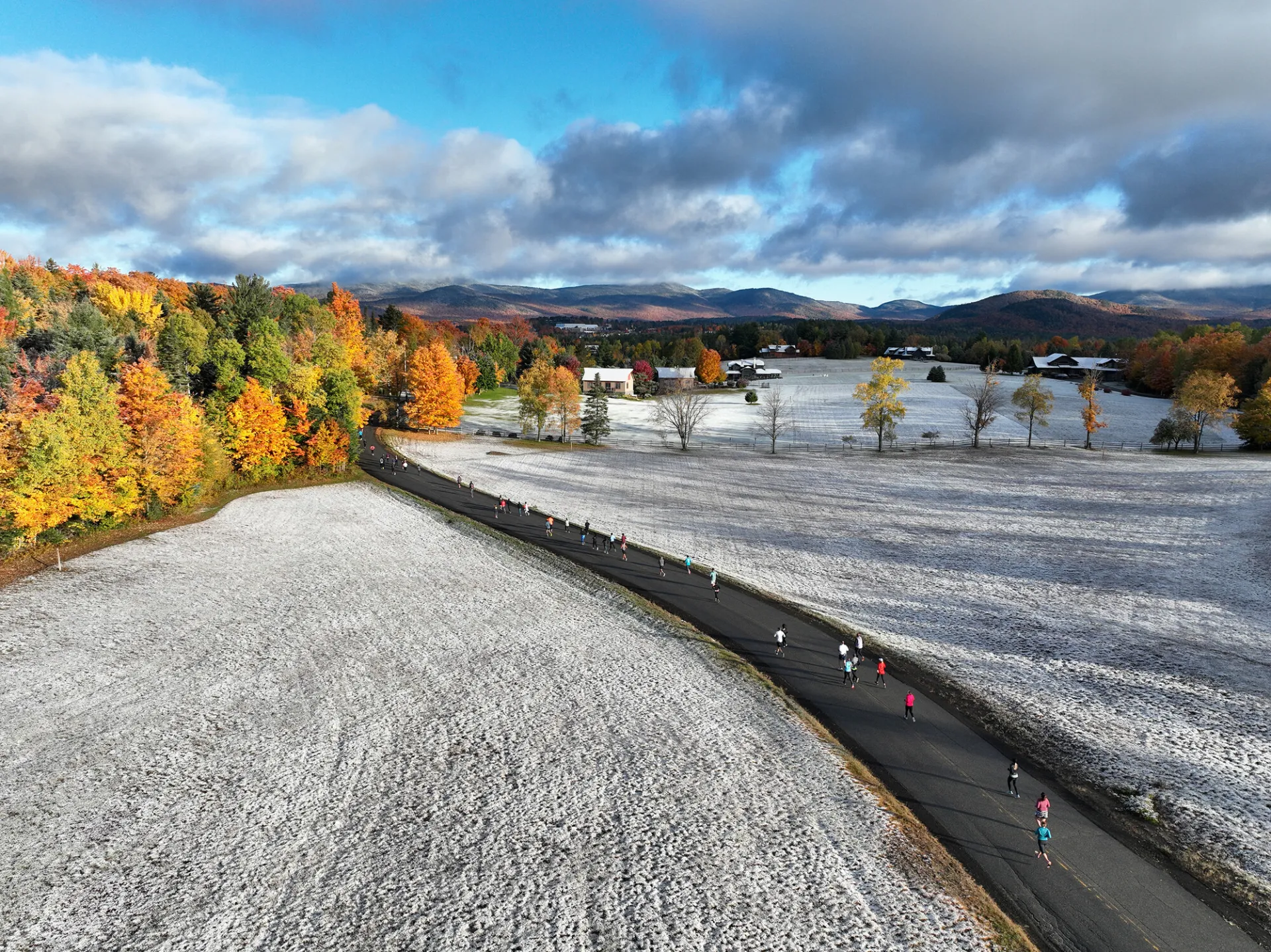 An aerial view of runners for the Lake Placid 10k running down a snow, fall foliage path.