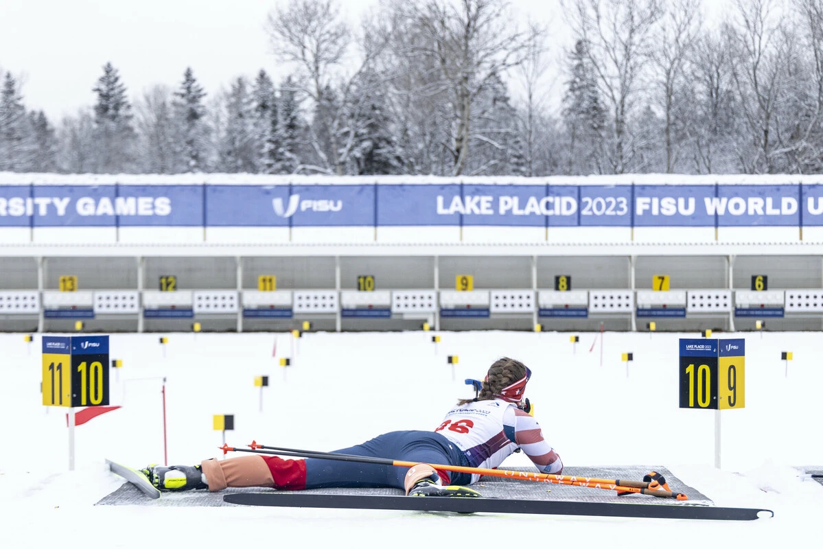 The image shows an athlete in a prone position, preparing to shoot.