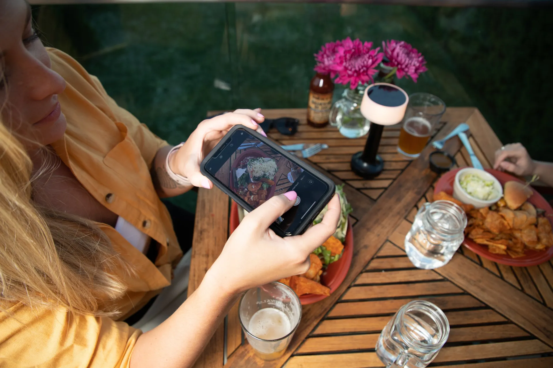 Looking down on a woman taking a photo of food on a restaurant table.